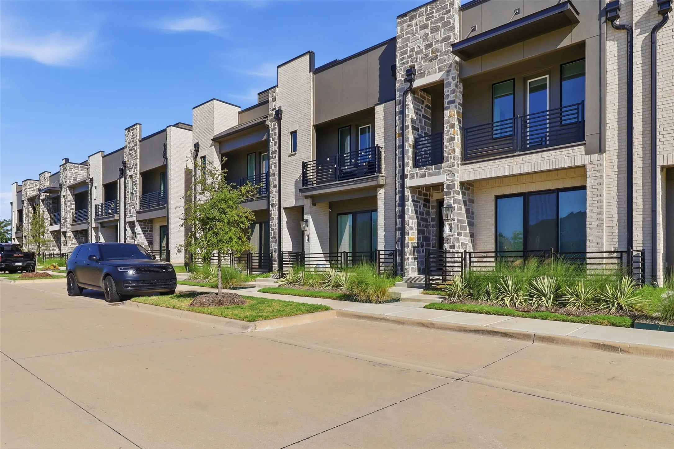 Contemporary townhome exterior featuring light-colored brick veneer, stone accents, black metal railings, and large windows