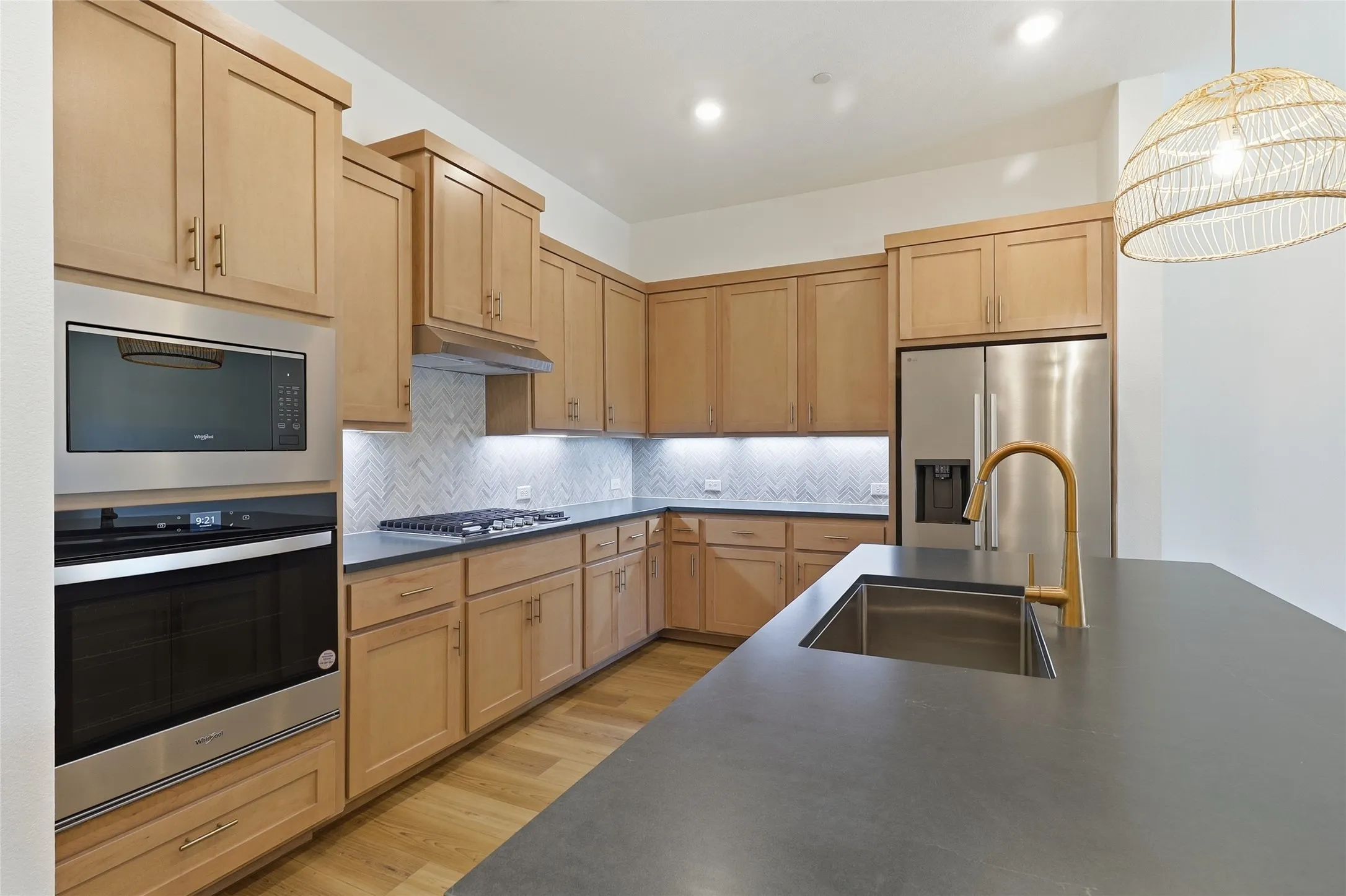Kitchen featuring light wood cabinetry, stainless steel appliances, herringbone tile backsplash, and dark countertops