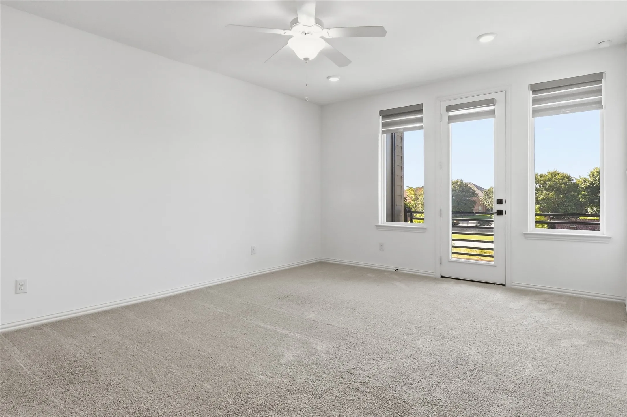 Spacious room featuring light-toned carpeting, white walls, and a ceiling fan with integrated lighting