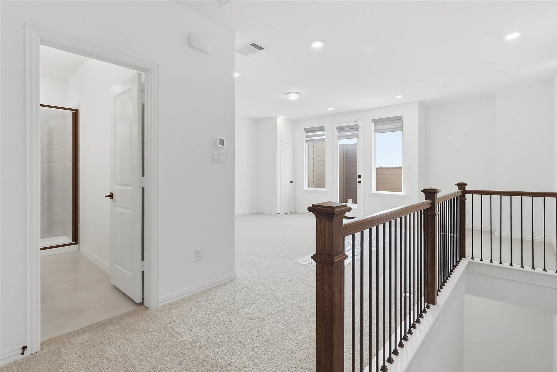 Upper-level landing featuring a wood and wrought iron railing, recessed lighting, and carpeted flooring