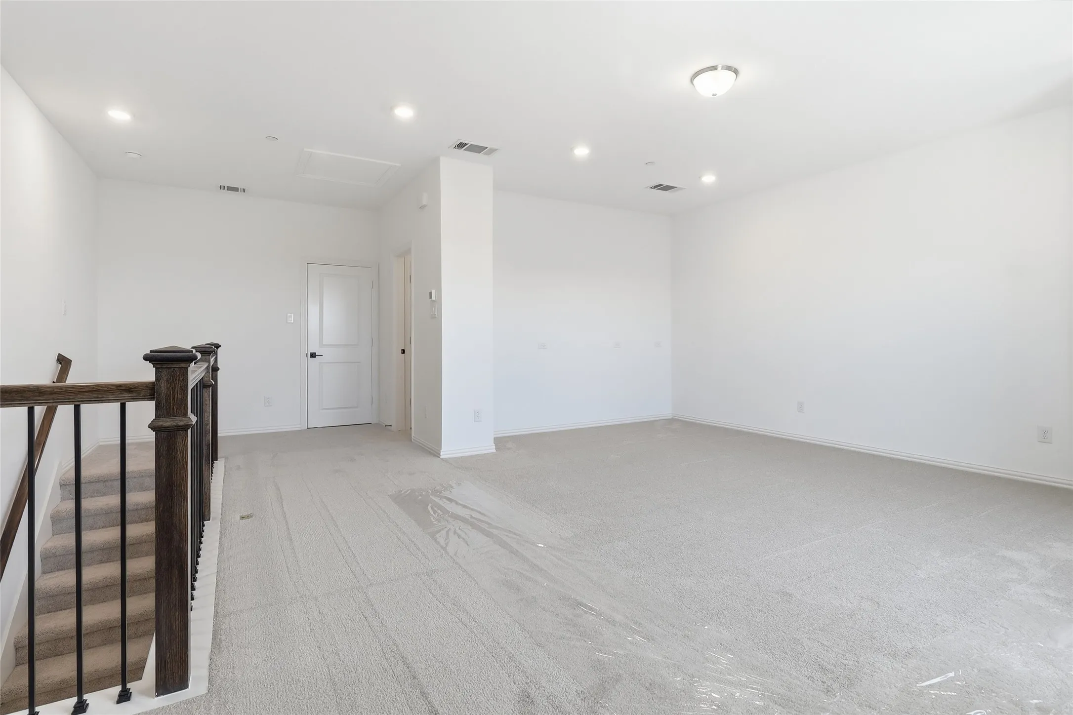 Spacious carpeted landing area with recessed lighting, an overhead flush-mount light fixture, and a dark wood and metal baluster railing
