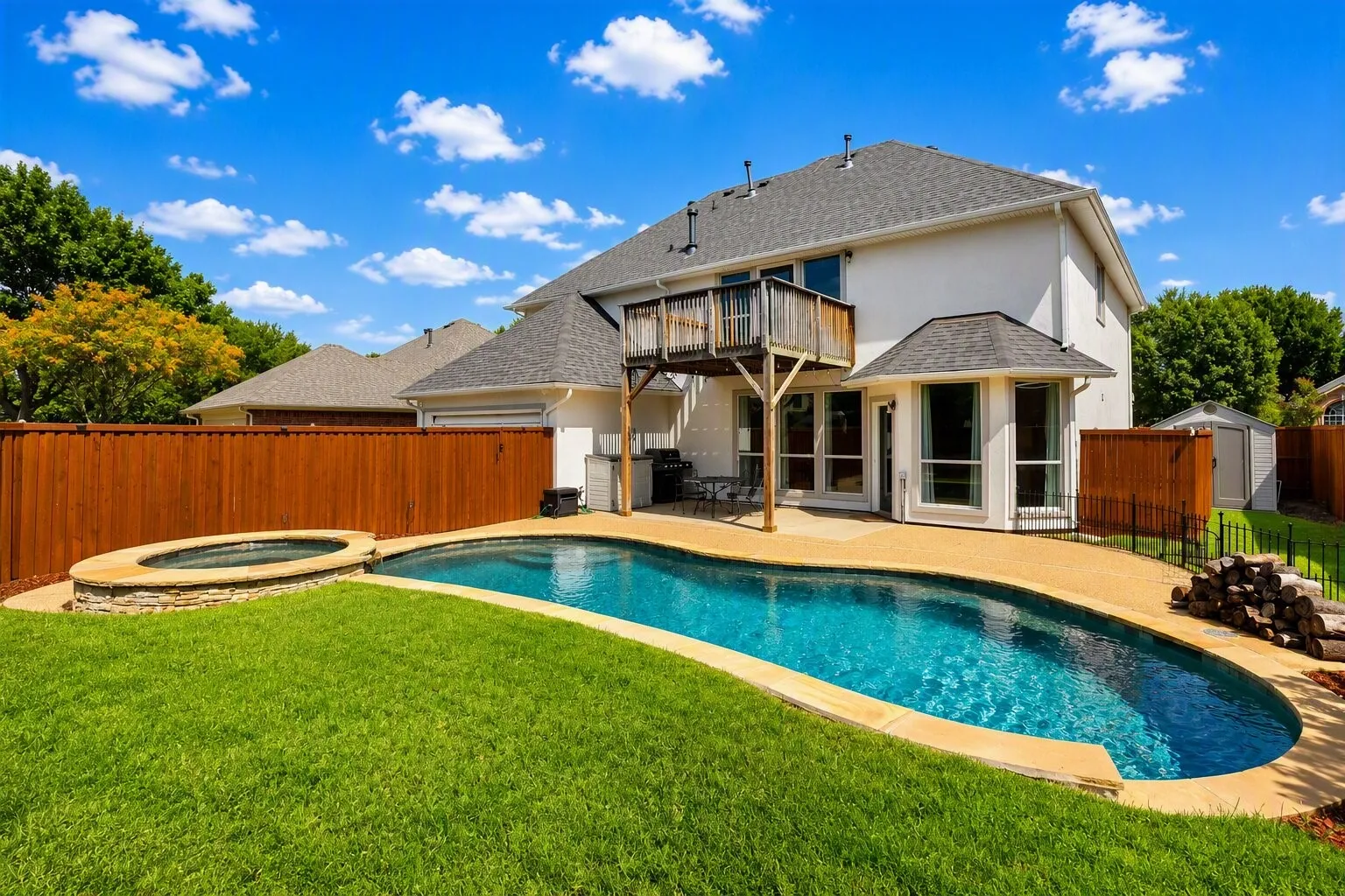 Expansive backyard featuring a curved swimming pool, a circular stone-clad spa, a private wood fence, a second-story wooden deck, and a detached storage shed