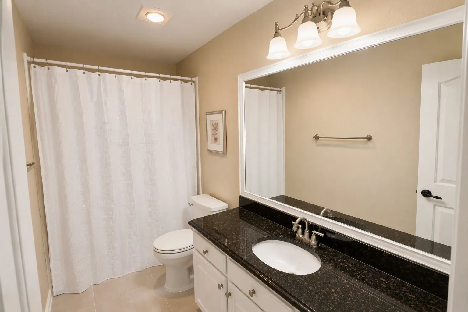 Bathroom featuring a vanity with dark granite countertop, undermount sink, brushed nickel faucet, large wall mirror, and white cabinetry