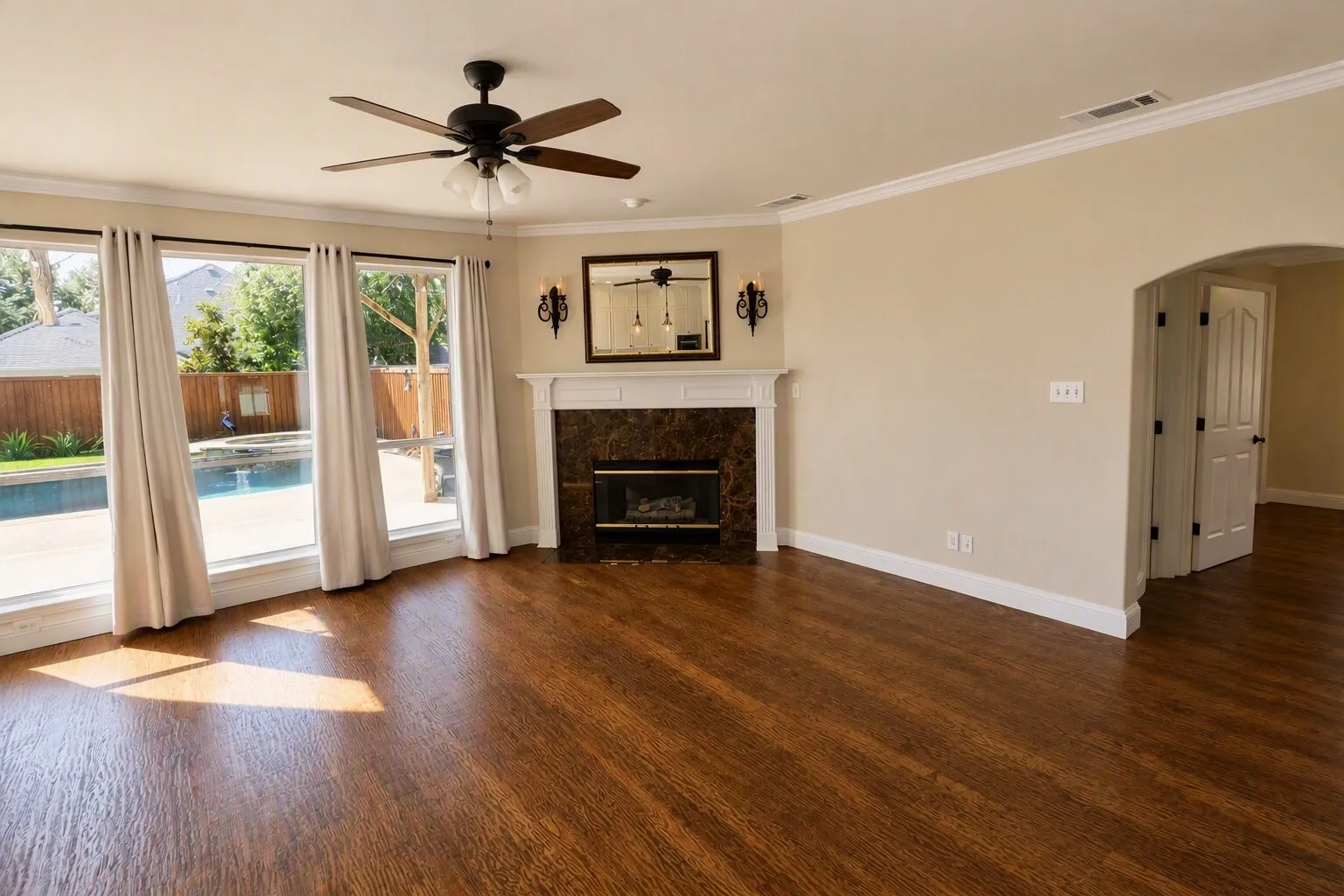 Hardwood flooring, a fireplace with a marble stone surround, a ceiling fan with integrated lighting, and multiple windows overlooking a swimming pool