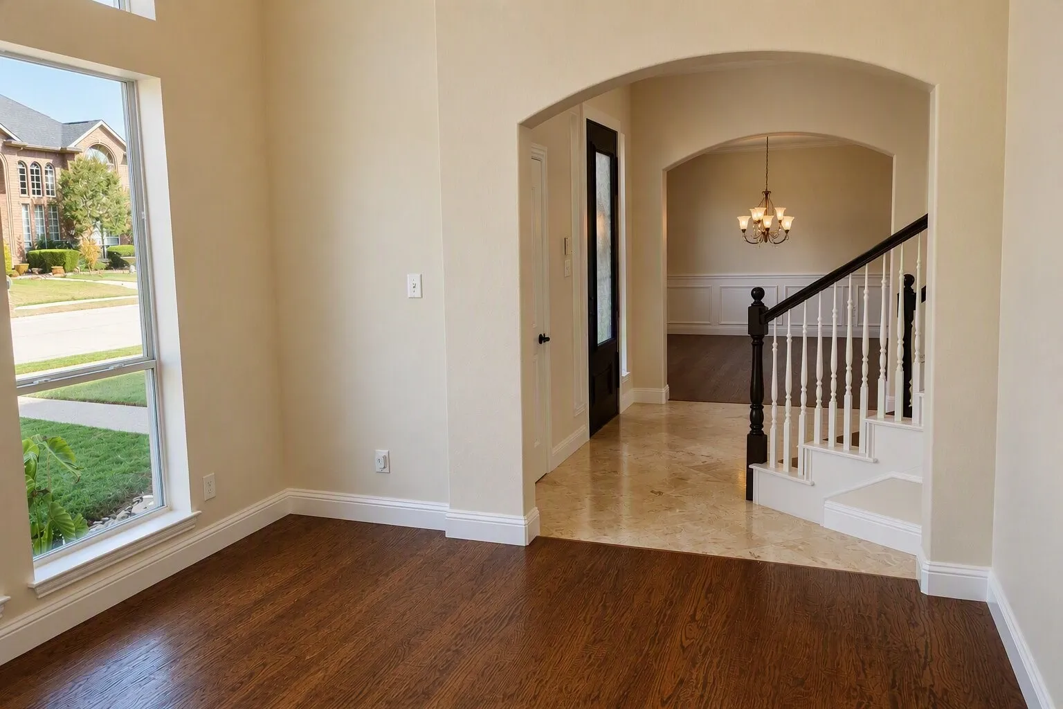 Hardwood flooring, staircase with white risers and dark wood handrail, arched doorway, tile flooring, and a multi-pane window