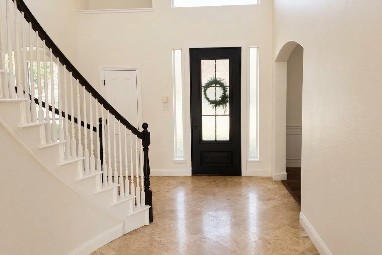 Two-story foyer featuring a curved staircase with dark wood handrail, light-toned tile flooring, and a dark-paneled iron door with glass inserts