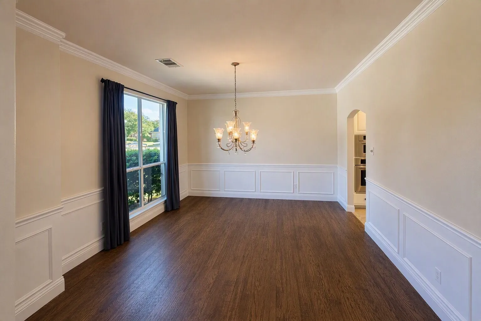 Hardwood flooring, wainscoting, crown molding, and a chandelier illuminate this spacious room