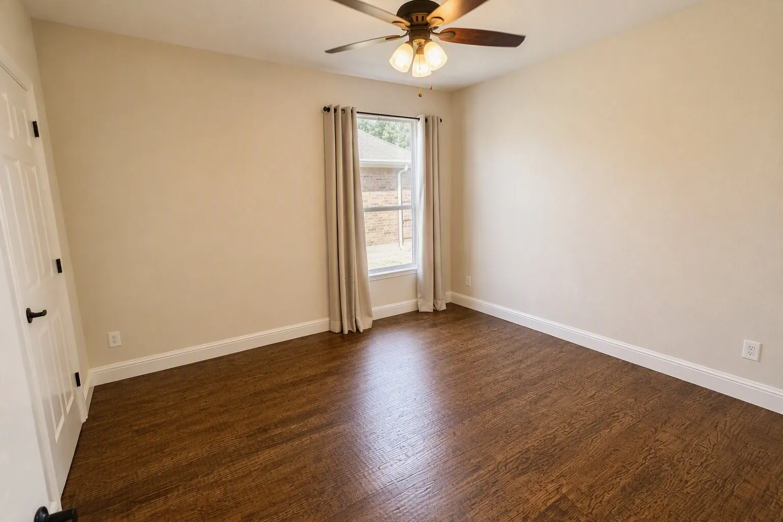 Hardwood flooring, ceiling fan with light fixture, neutral wall paint, white trim, and a window with drapery rods