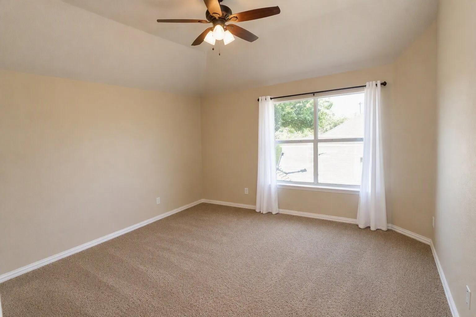 Carpeted flooring, vaulted ceiling, ceiling fan with integrated lighting, window with white trim, and neutral wall tones