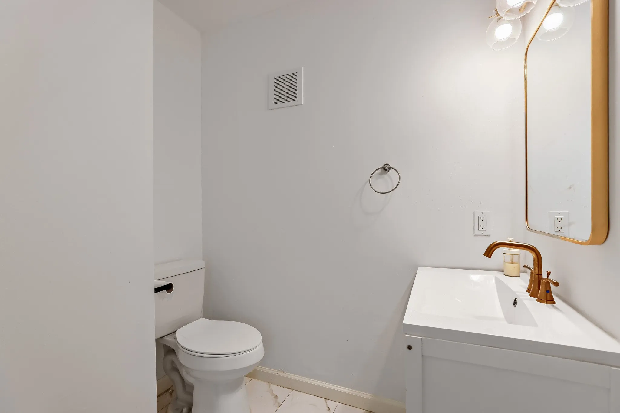 Half bath, Contemporary vanity with a white countertop and integrated sink, complemented by a brass-toned faucet and a framed mirror