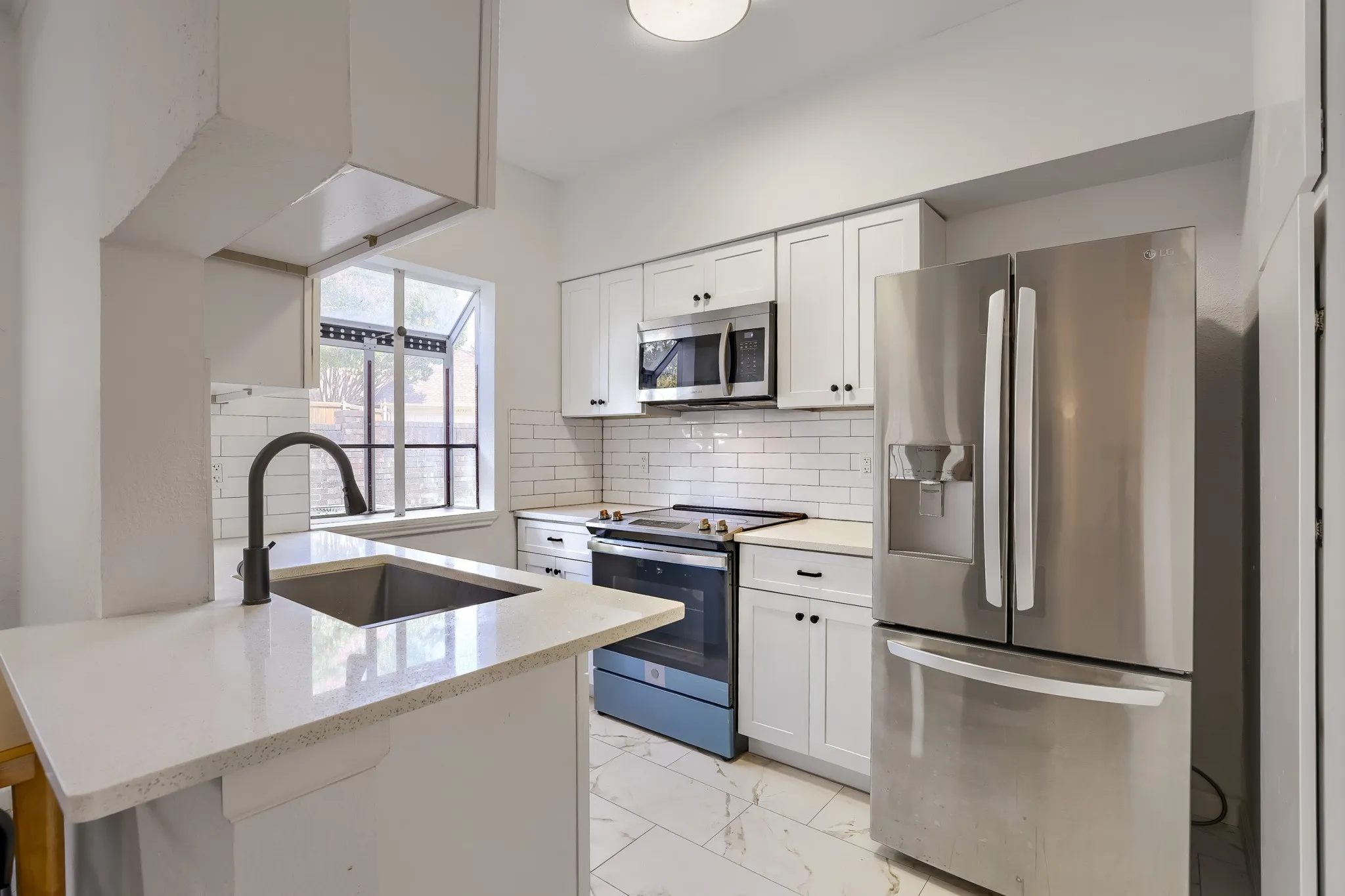 Modern kitchen featuring white shaker cabinetry, stainless steel appliances, a subway tile backsplash, light-toned countertops, and a contemporary dark-finish faucet