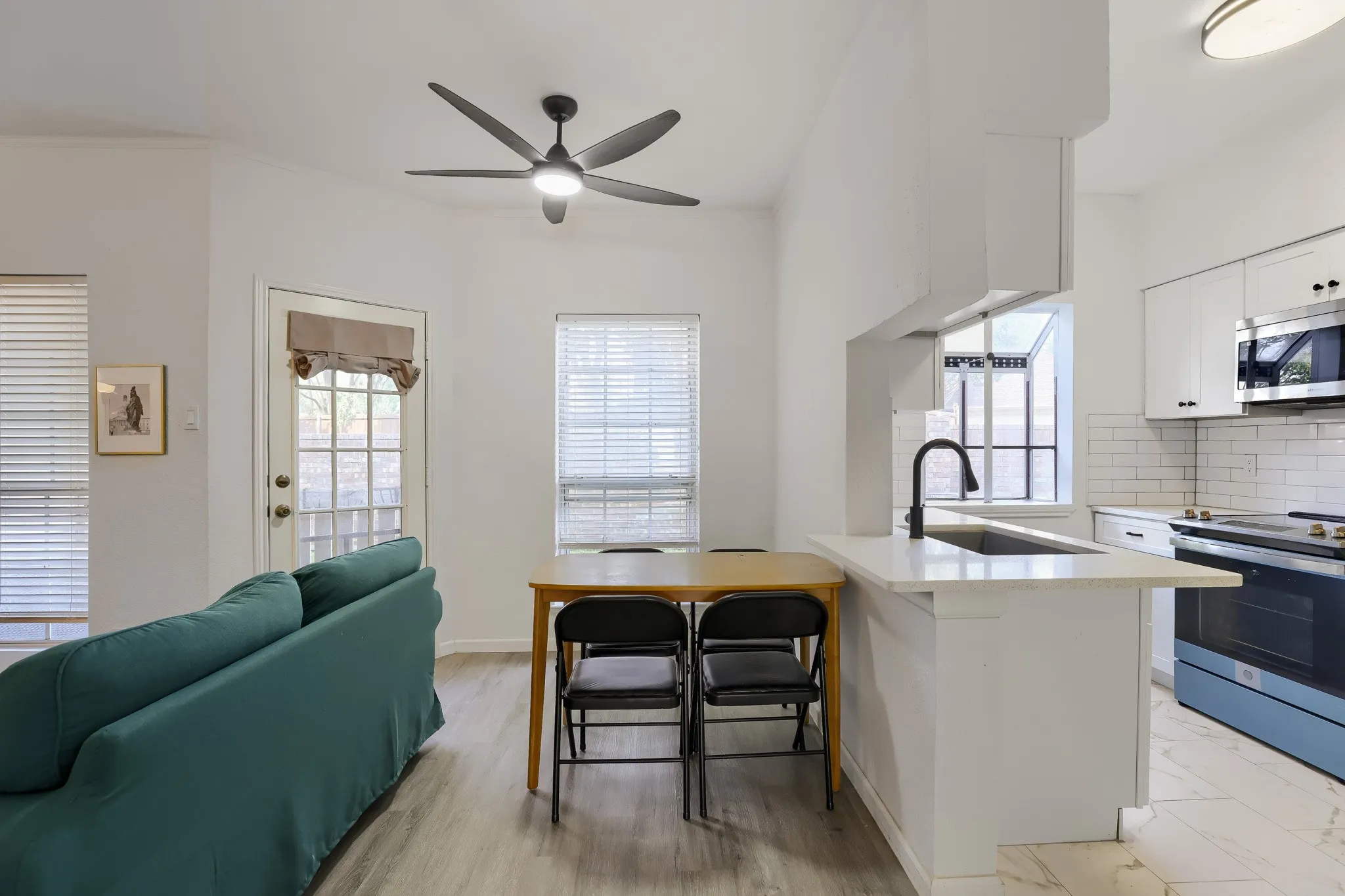 Open-concept living space featuring wood-finish flooring, a contemporary ceiling fan, and a kitchen island with a built-in sink and a modern matte black faucet