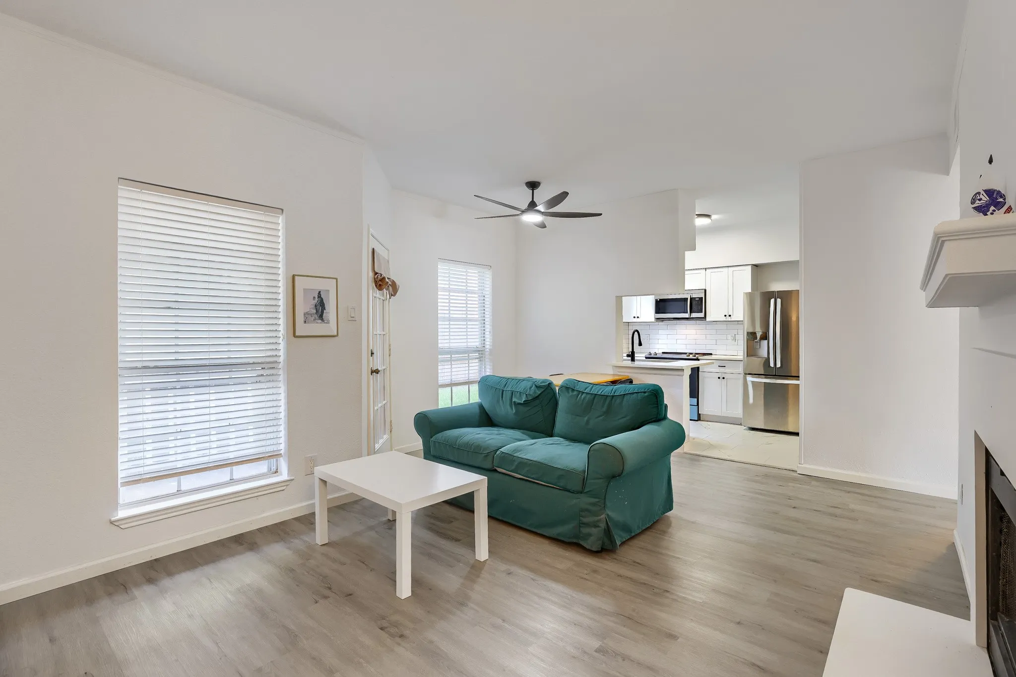 Living area with light wood-finish flooring, white walls, and a ceiling fan