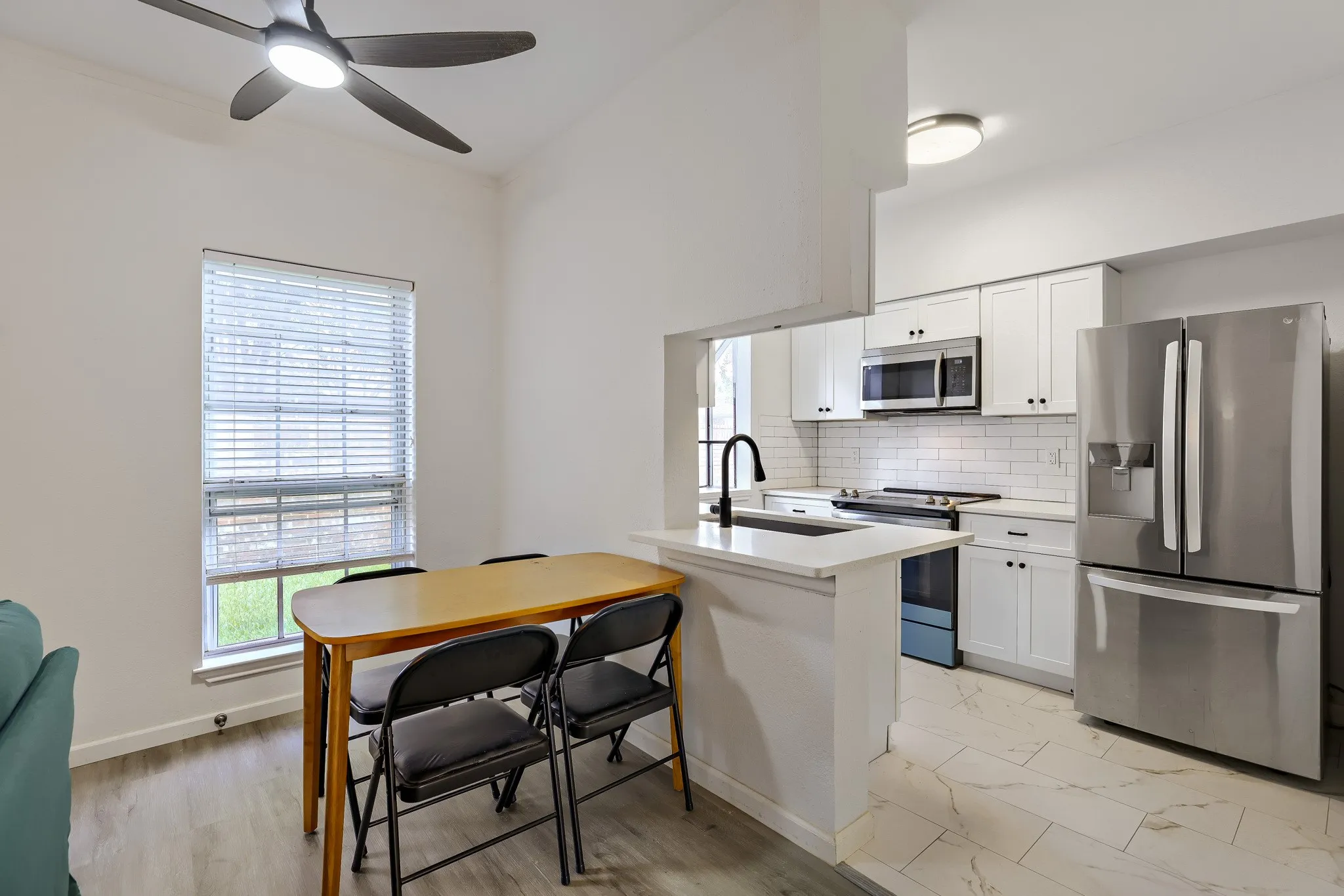 Bright kitchen and dining area featuring white cabinetry, subway tile backsplash, stainless steel appliances, and a breakfast bar
