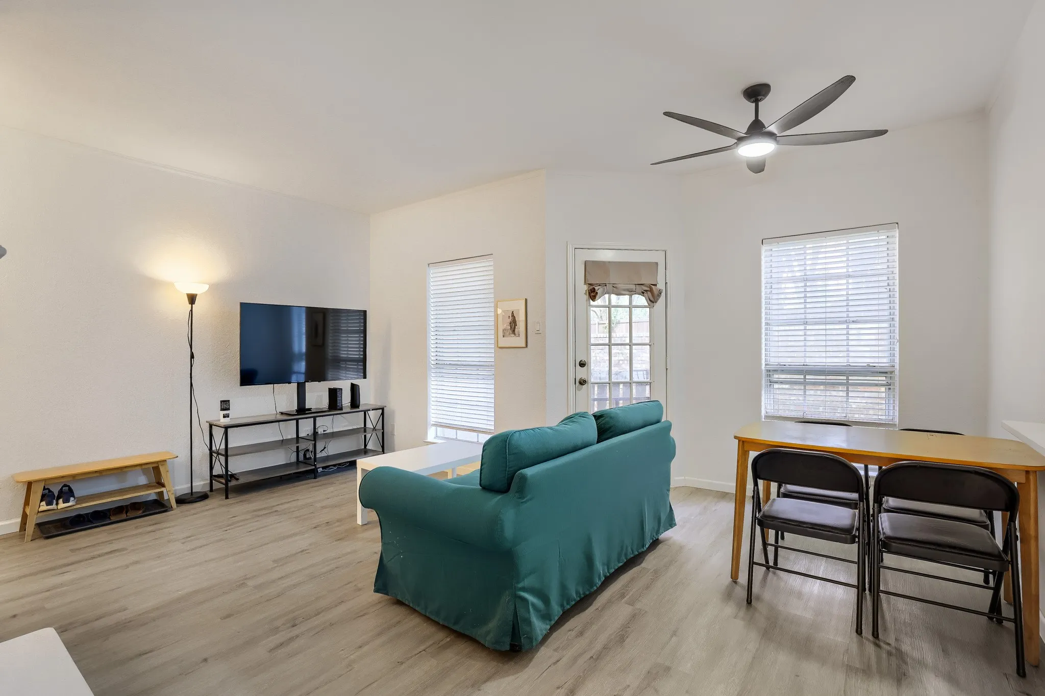Open-concept living area featuring light wood-finish flooring, white walls, and a modern ceiling fan