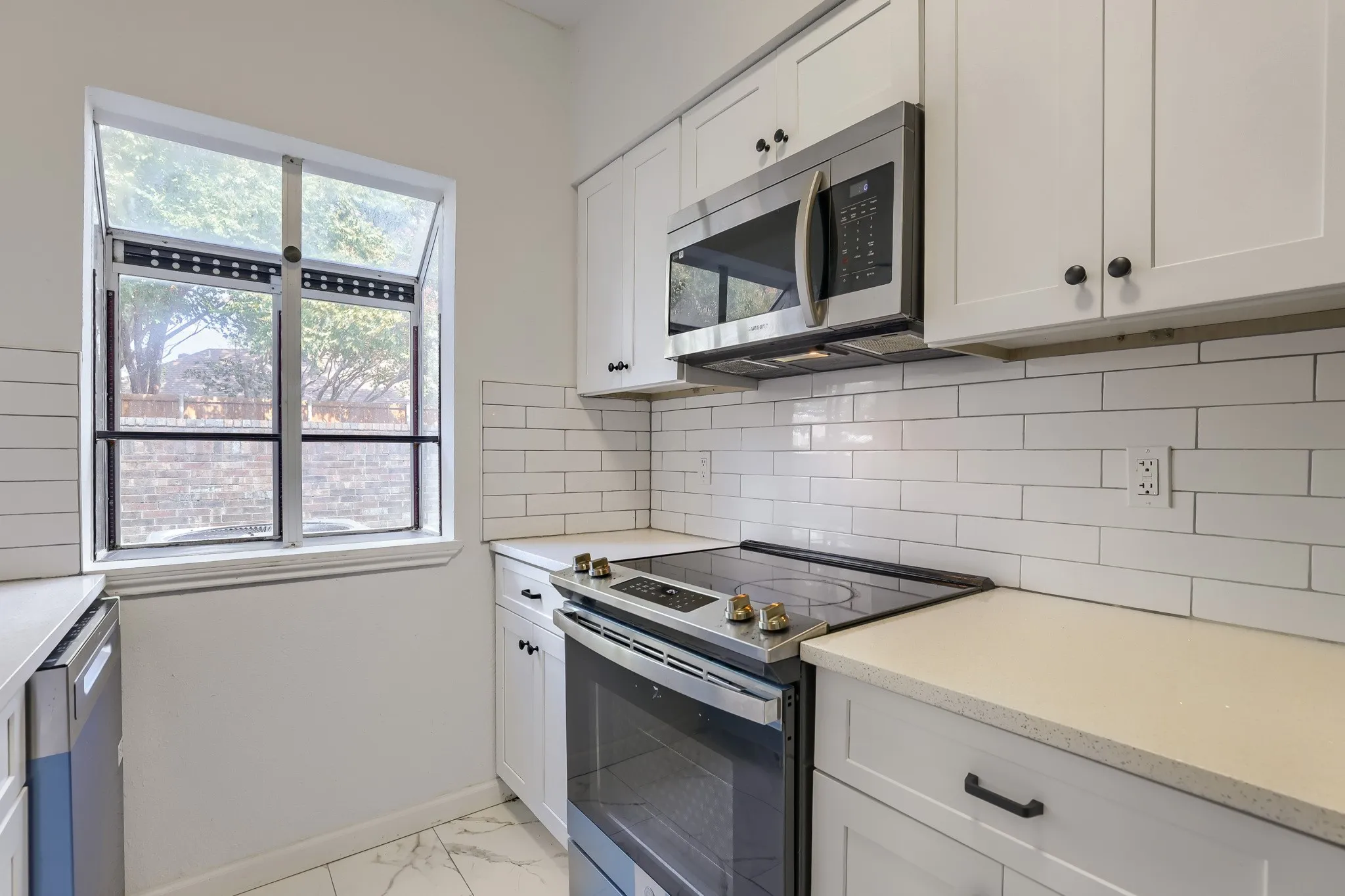 Modern kitchen featuring white shaker cabinetry, stainless steel appliances, light-toned countertops, subway tile backsplash, and wood-finish flooring