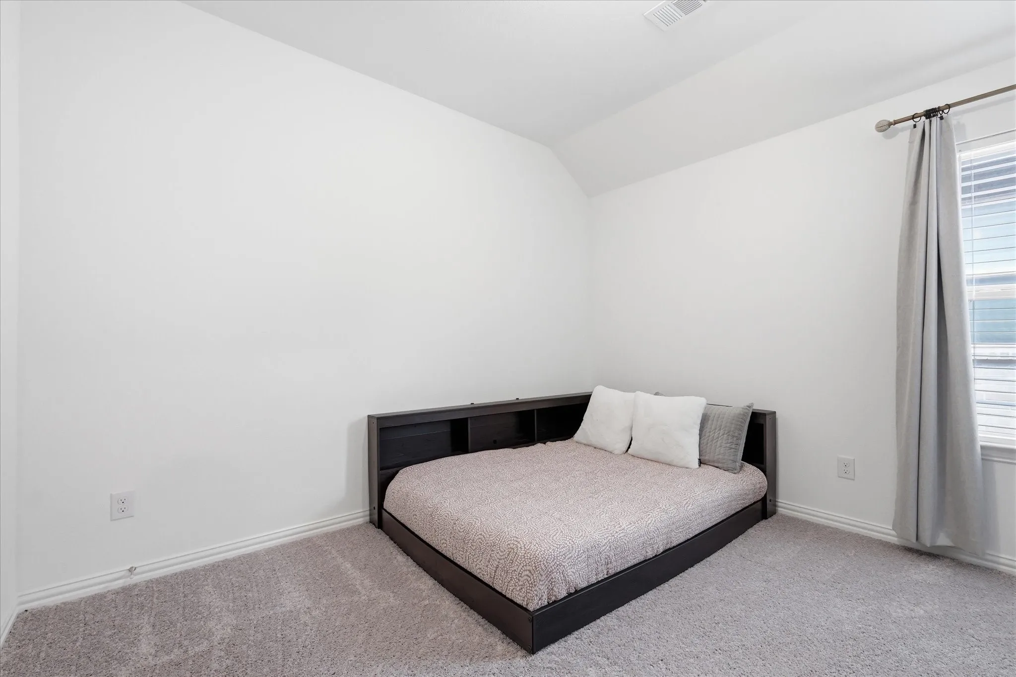 Carpeted room with a vaulted ceiling and white baseboards