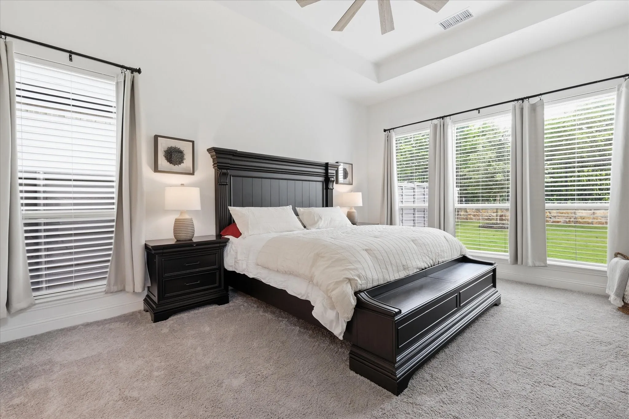 Carpeted room featuring a tray ceiling with a ceiling fan, multiple windows with blinds, and white walls