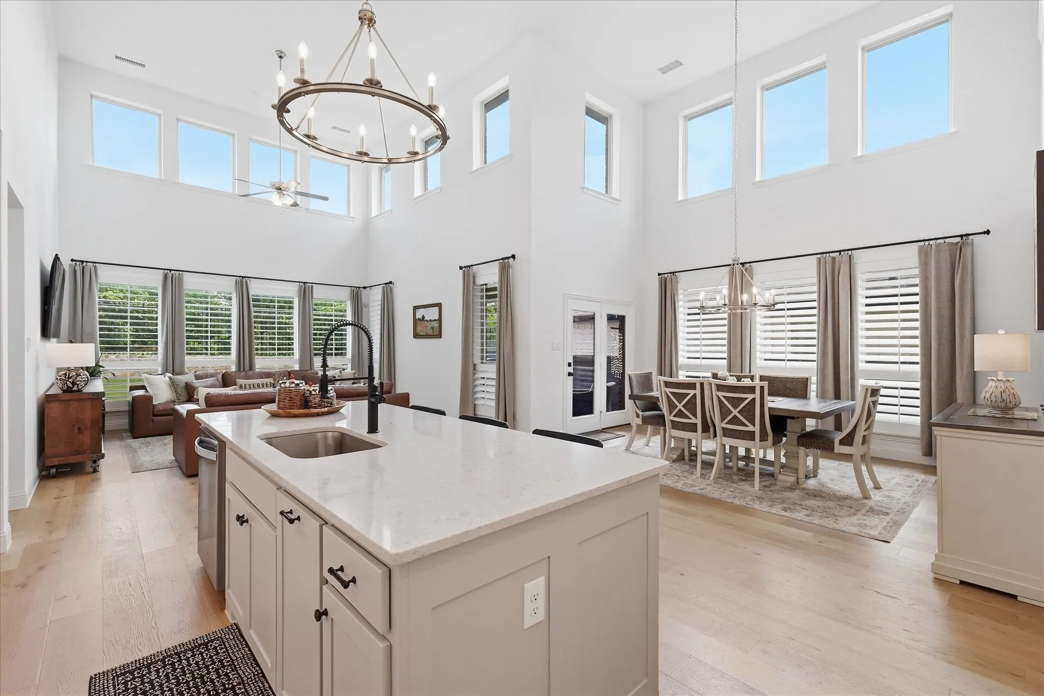 Gourmet kitchen island with an undermount sink and matte black faucet, open to a two-story living space featuring high windows, wood-finish flooring, and a formal dining area