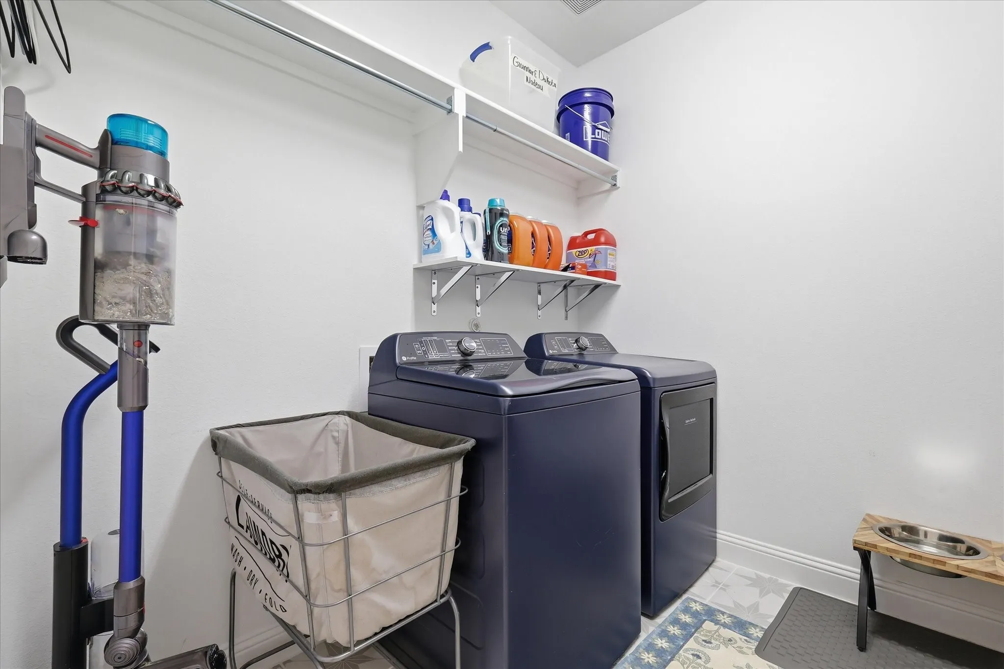 Dedicated laundry area featuring a white floating shelf, white wall-mounted shelving, and light-toned flooring