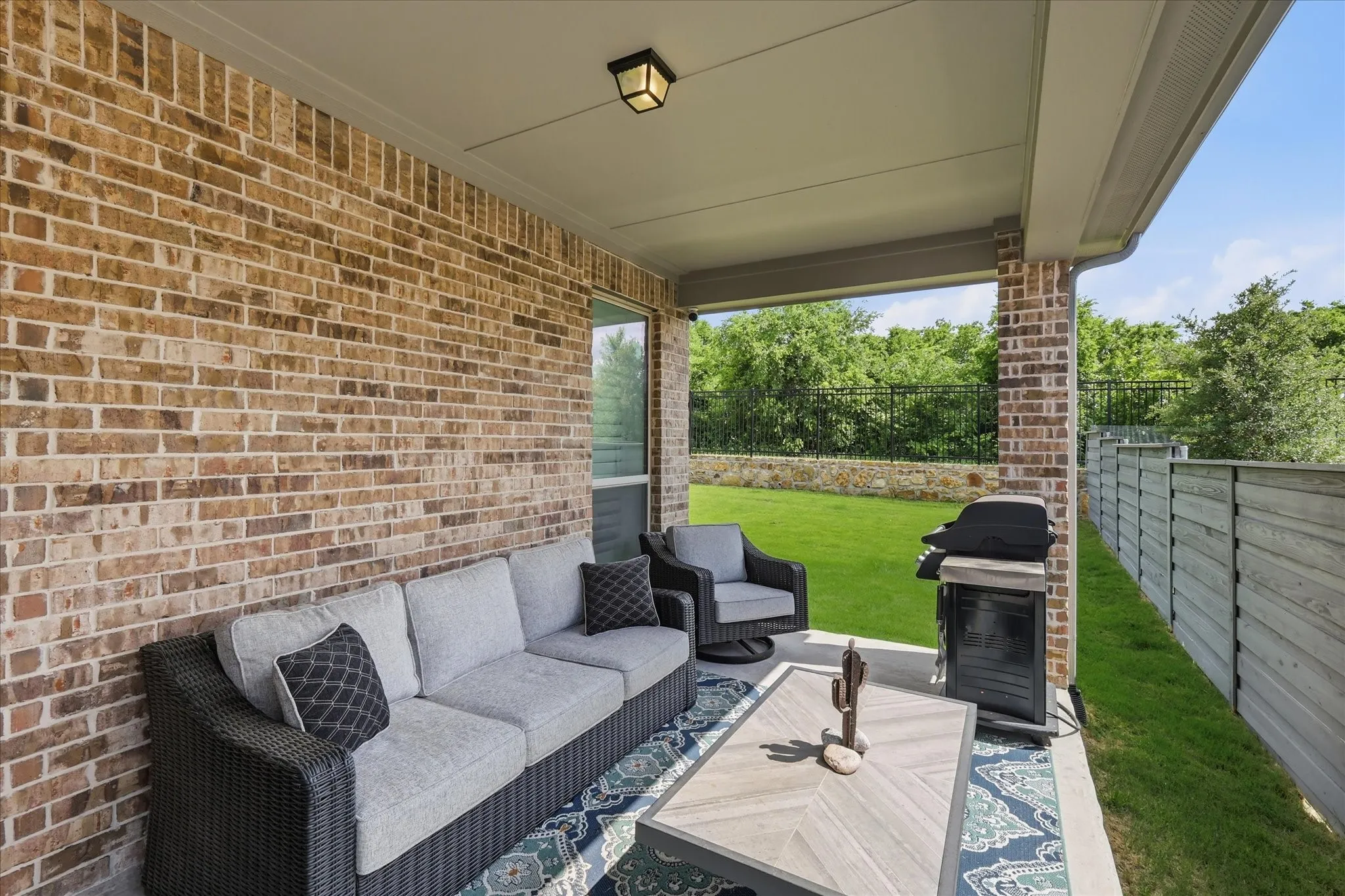 Covered patio featuring a brick exterior wall, concrete flooring, and a flat panel privacy fence