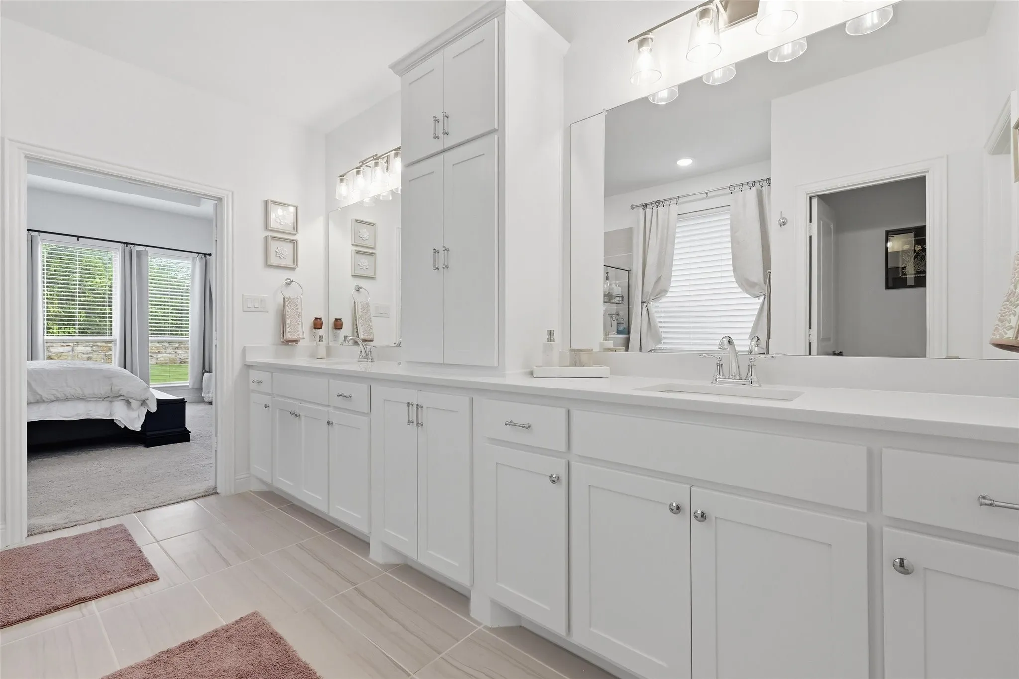 Bathroom vanity featuring dual sinks, white cabinetry, a large mirror, and overhead vanity lighting