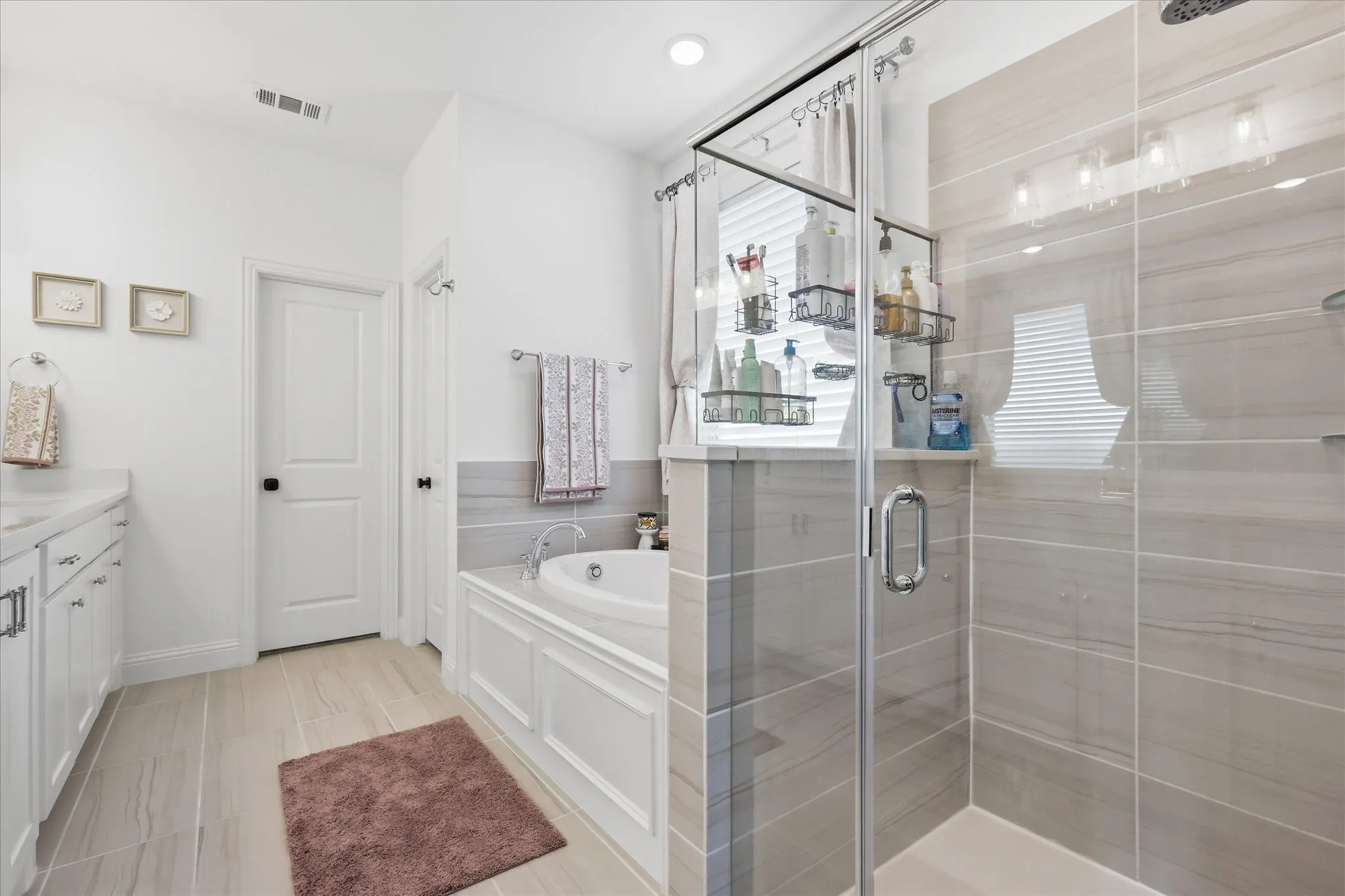Spacious bathroom featuring a glass-enclosed shower, built-in soaking tub, wood-finish flooring, white vanity with integrated sink, and white paneled doors