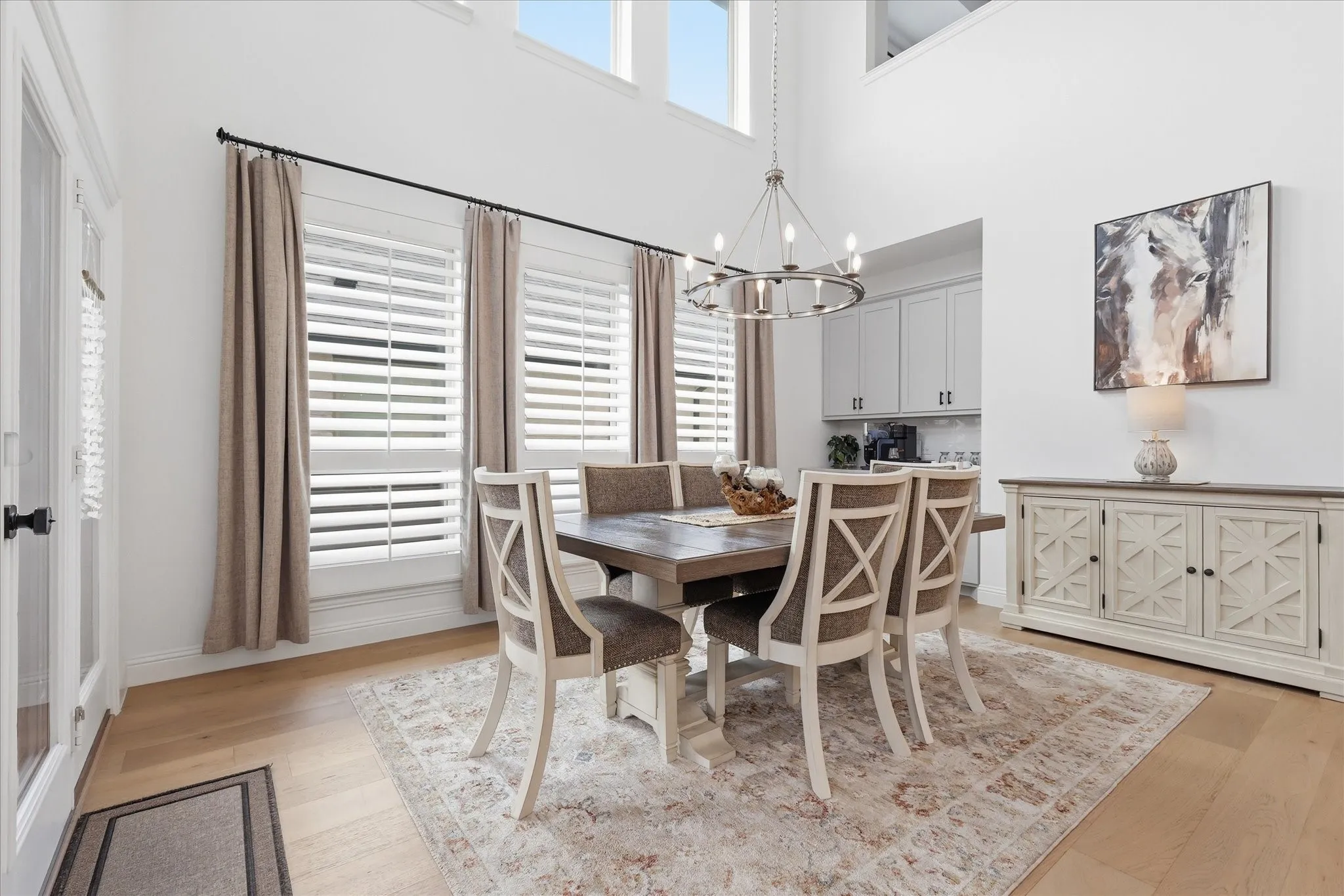 High ceilings define this dining area, featuring hardwood flooring and a prominent chandelier