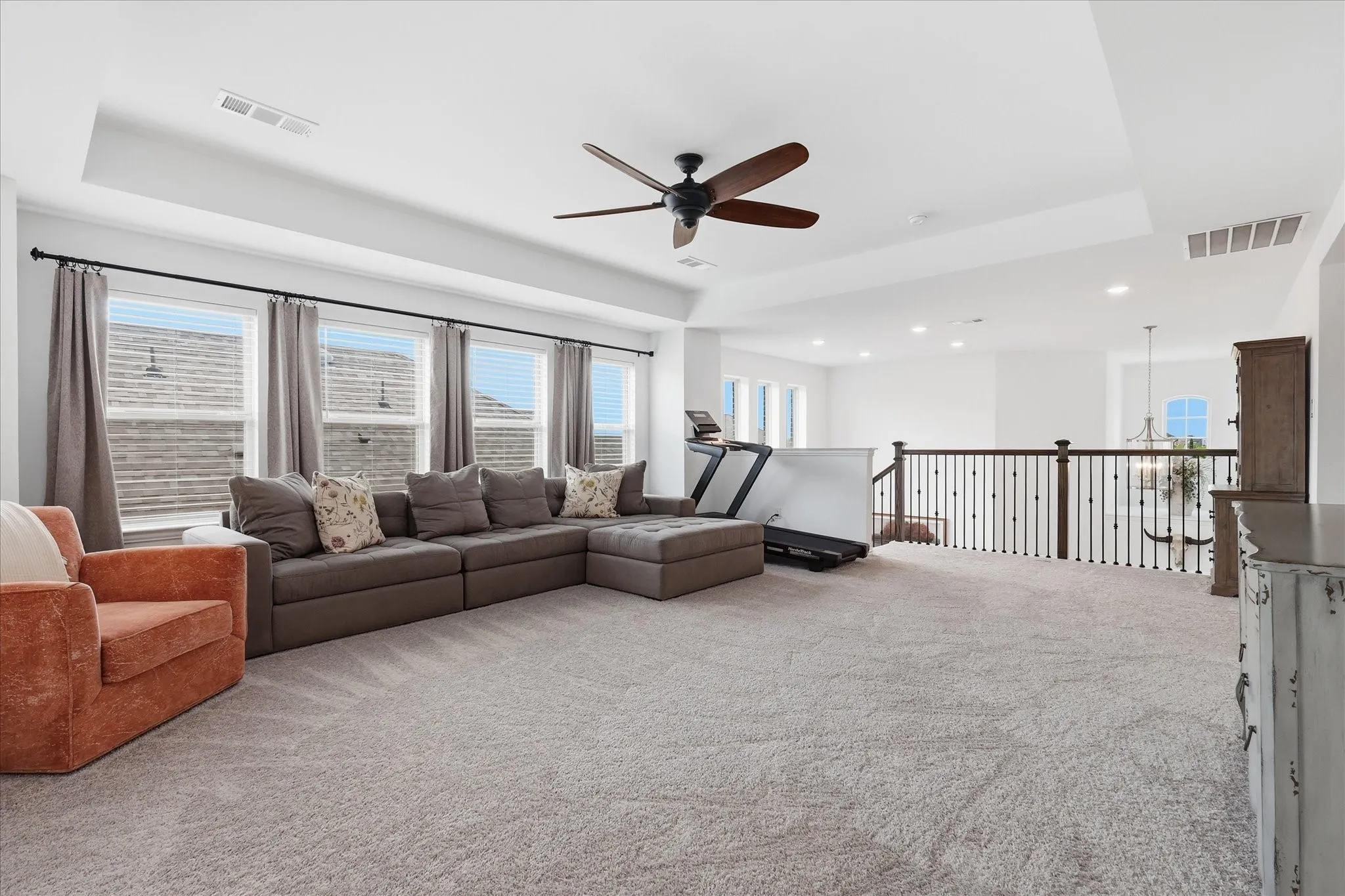 Spacious carpeted loft area with a tray ceiling and a ceiling fan
