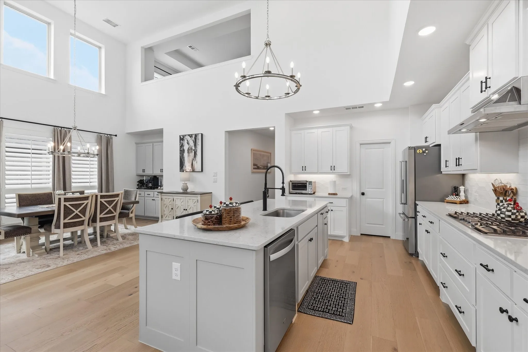 Open-concept kitchen and dining area featuring a central island with a sink, white cabinetry, integrated stainless steel appliances, and wood-finish flooring
