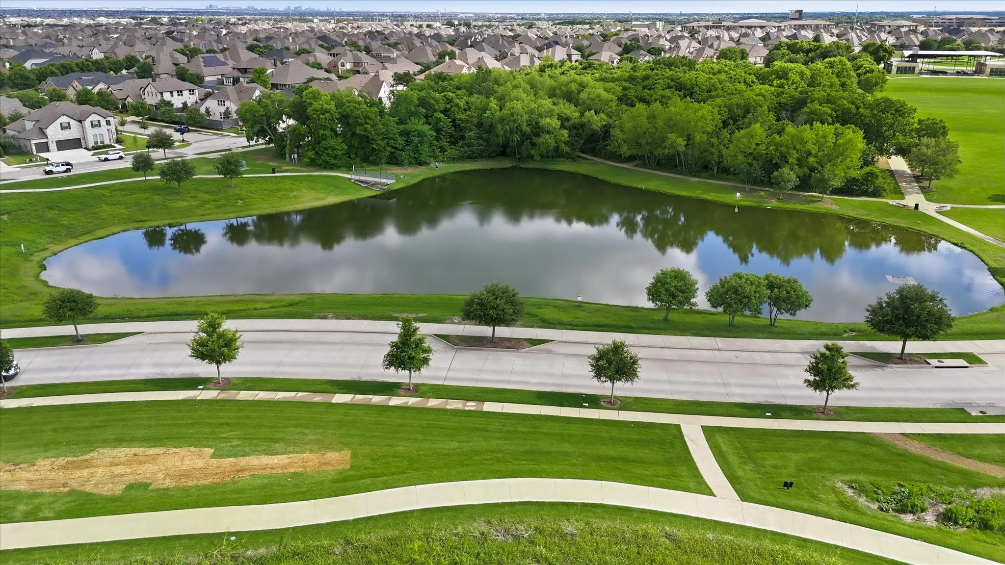Community lake with surrounding green spaces, mature trees, and pedestrian pathways