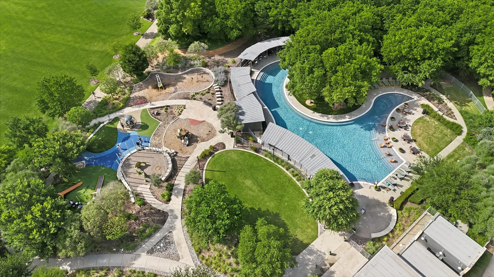 Expansive community amenity area featuring a large resort-style pool with various depths, surrounding lounge areas, and multiple shade structures