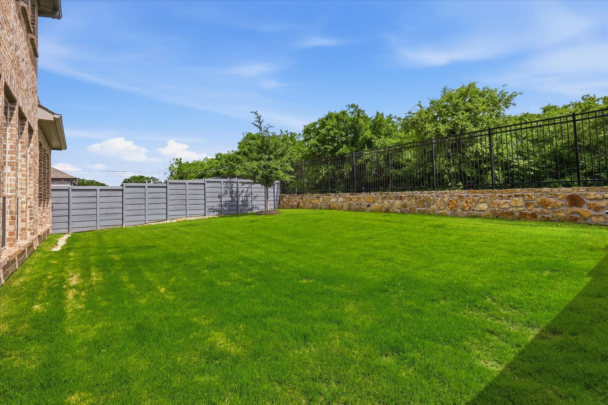 Expansive green lawn framed by a stone retaining wall and black wrought iron fencing