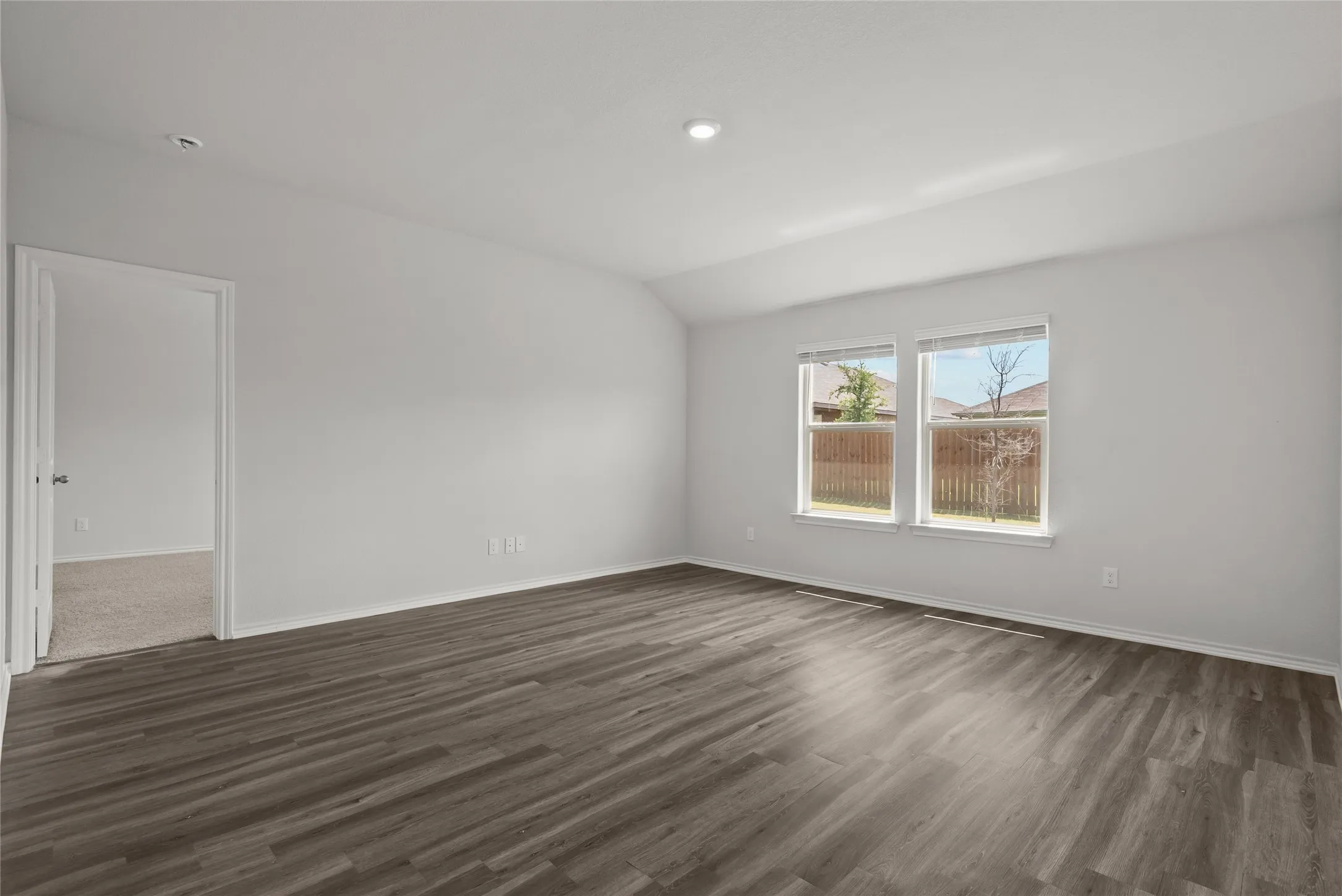 Spacious room featuring wood-finish flooring, light neutral wall paint, two windows, and a recessed ceiling light
