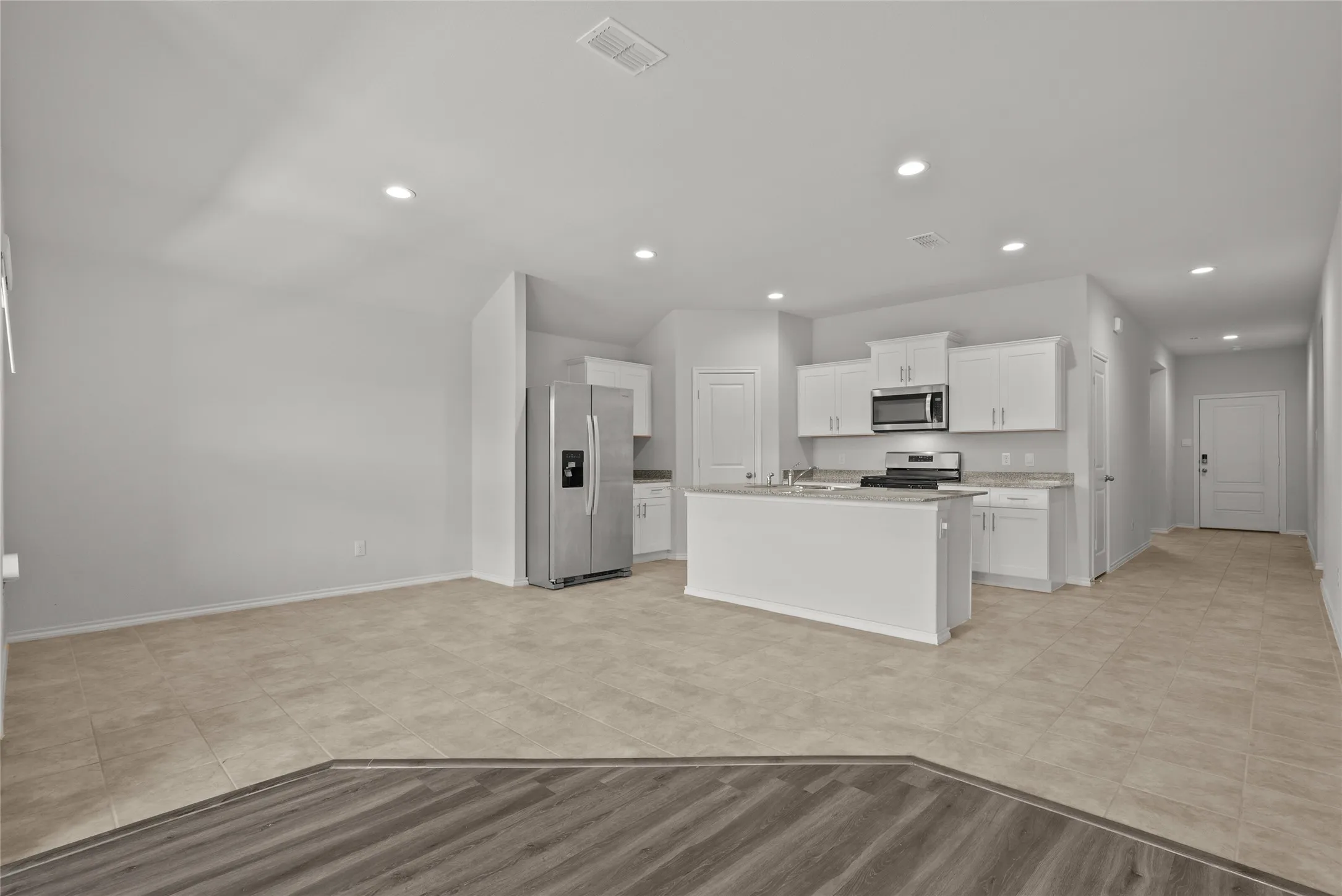Open-concept living space featuring a modern kitchen with a central island, white cabinetry, stainless steel appliances, and recessed lighting