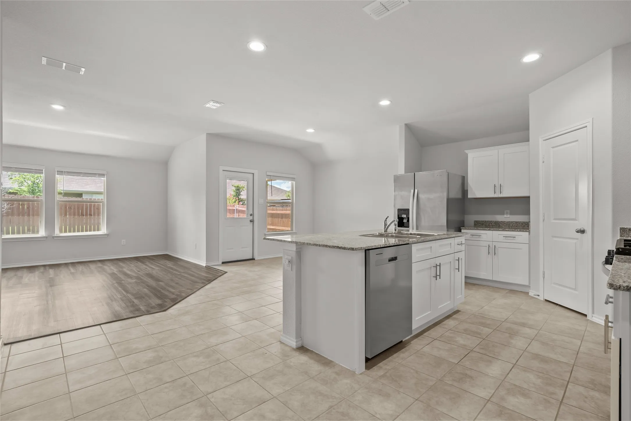 Open-concept kitchen featuring an island with a stainless steel sink and dishwasher, white cabinetry, and granite countertops