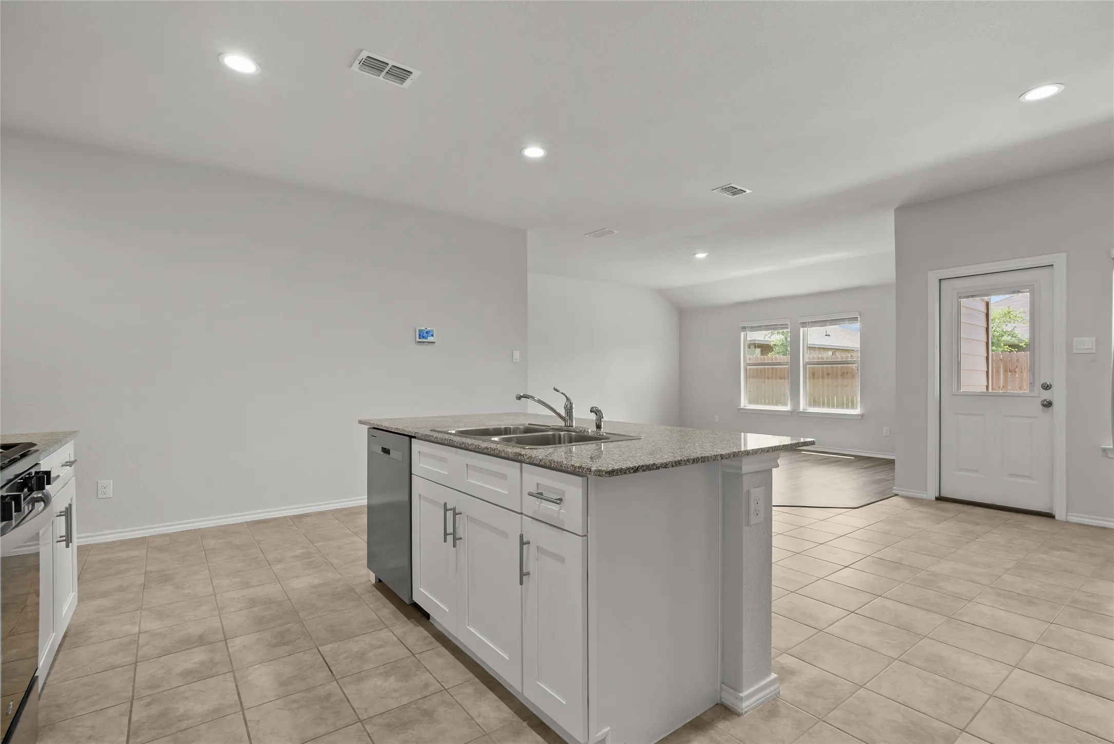 Kitchen island featuring an undermount double sink, integrated dishwasher, and granite-finish countertop