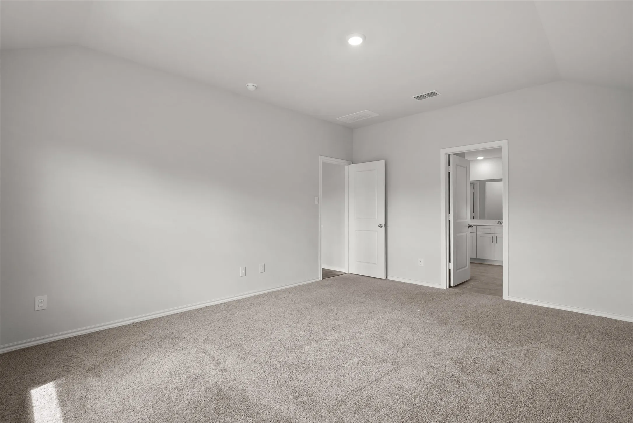 Spacious room featuring vaulted ceilings, light gray wall paint, and plush carpet flooring