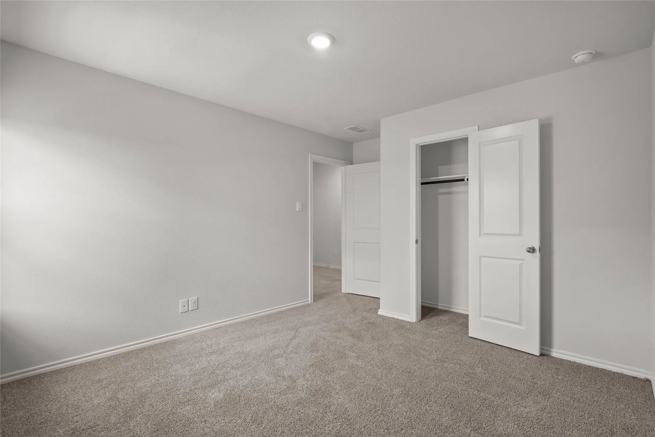 Spacious room featuring neutral carpeting, light-toned walls, recessed lighting, and a built-in closet with bi-fold doors
