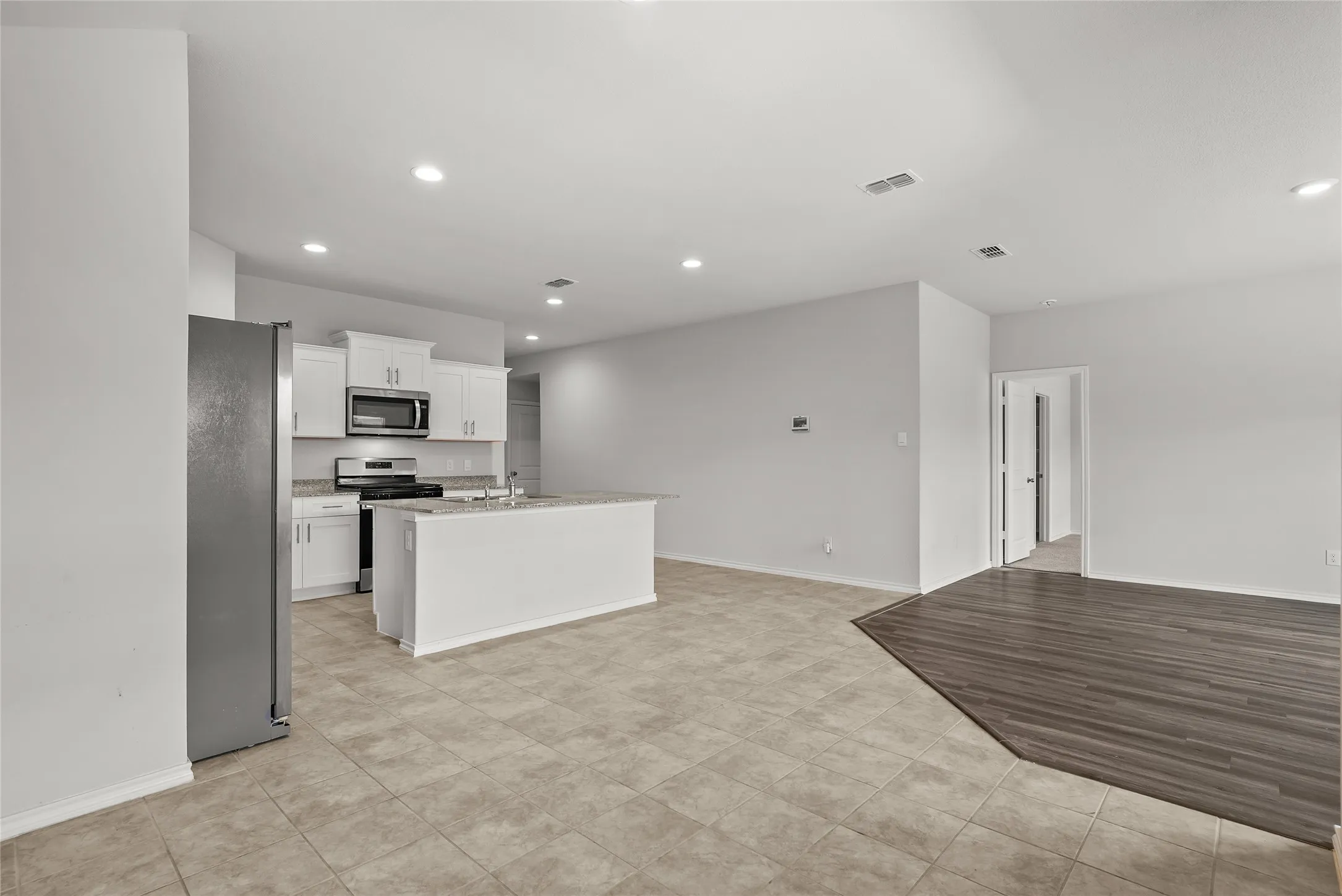 Open-concept kitchen and living area featuring white cabinetry, stainless steel appliances, a center island with a sink, recessed lighting, and a combination of tiled and wood-finish flooring