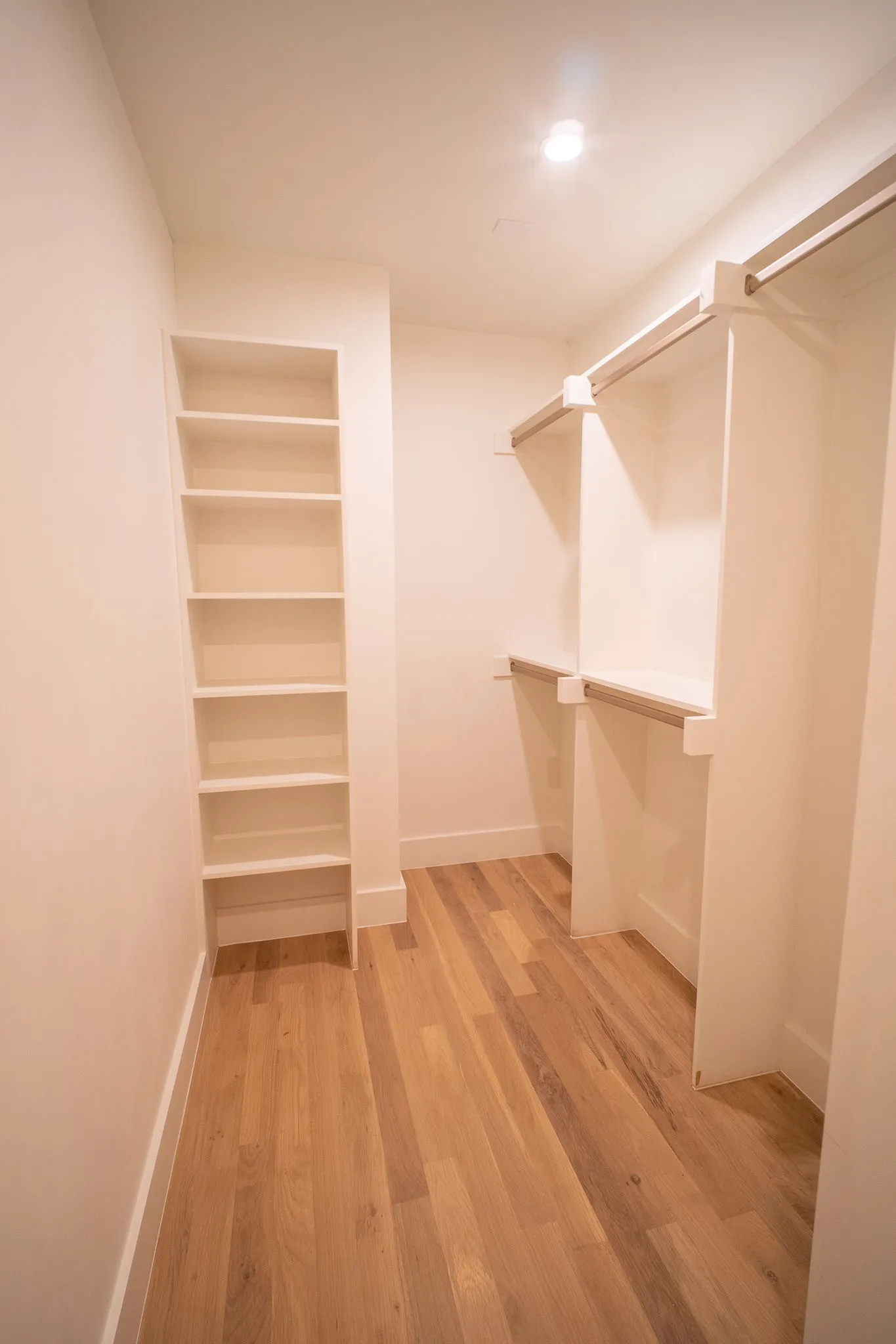 This closet features hardwood floors, built-in shelving, and hanging rods