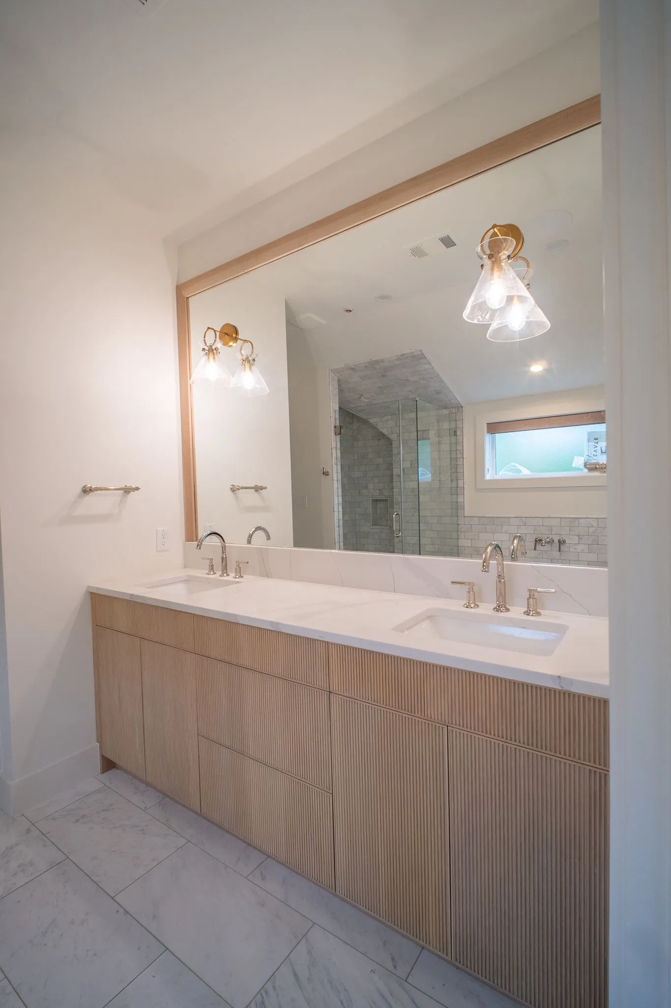 Bathroom featuring a light wood dual vanity with two integrated sinks, brushed nickel faucets, and a large wall-mounted mirror