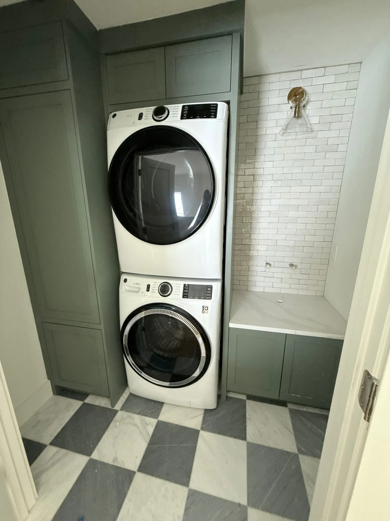 Laundry area featuring green cabinetry, a white subway tile backsplash, and a checkerboard floor