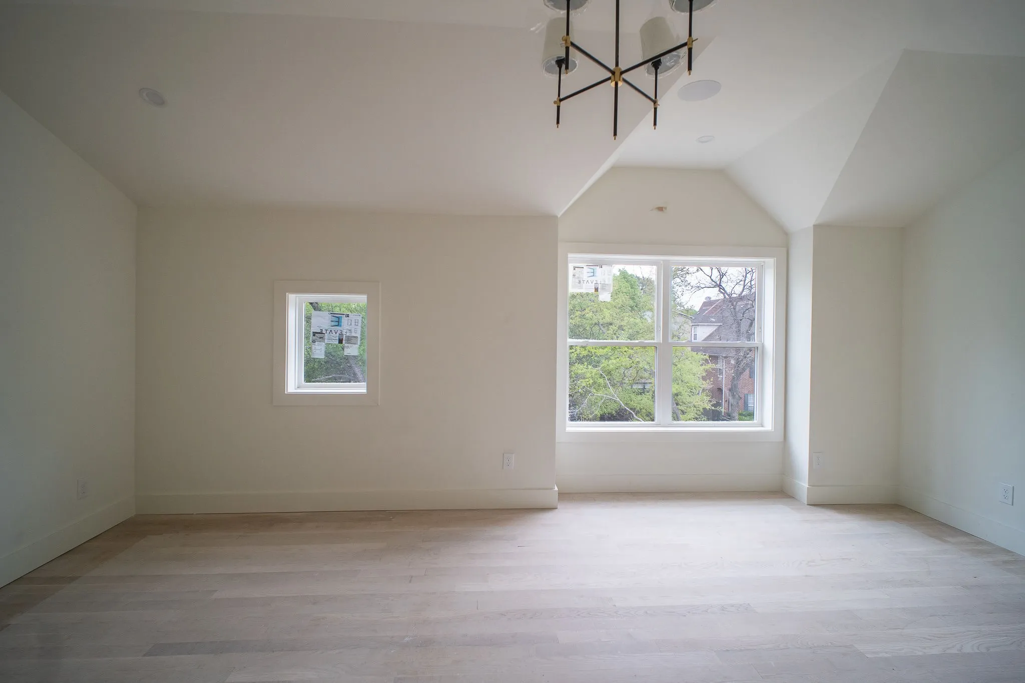 Spacious room featuring light-colored hardwood flooring, white walls, and a large window providing views of trees and other properties