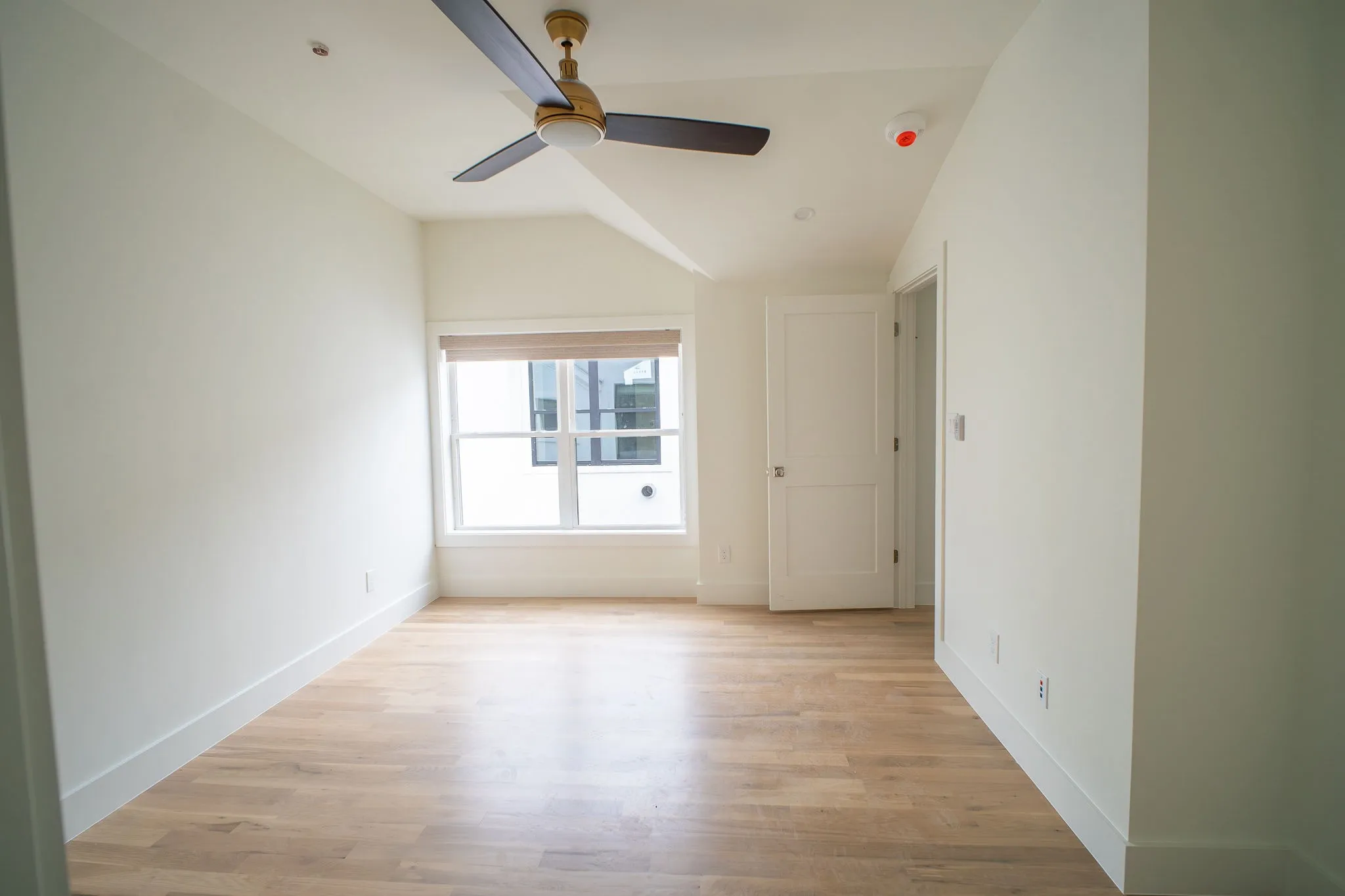 Spacious room featuring hardwood flooring, a ceiling fan, and a window with blinds