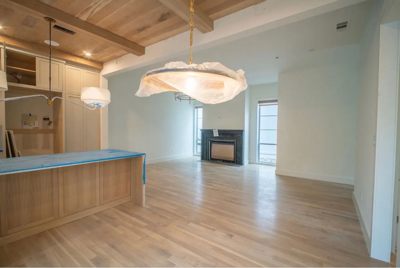 This open-concept space features hardwood floors, a wood beam ceiling, and a fireplace with a dark stone surround