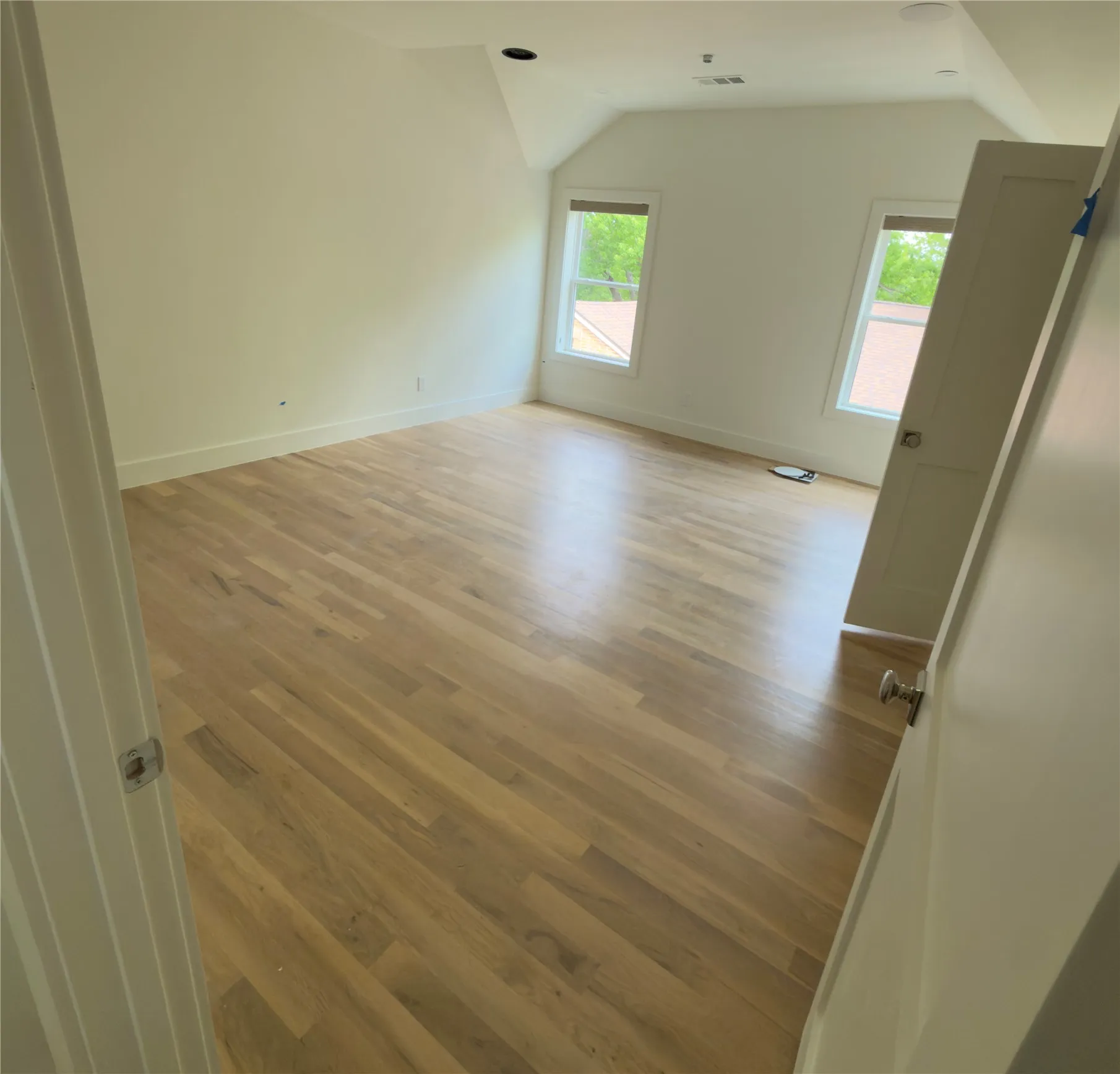 Spacious room featuring hardwood flooring, white walls, and two windows providing ample natural light