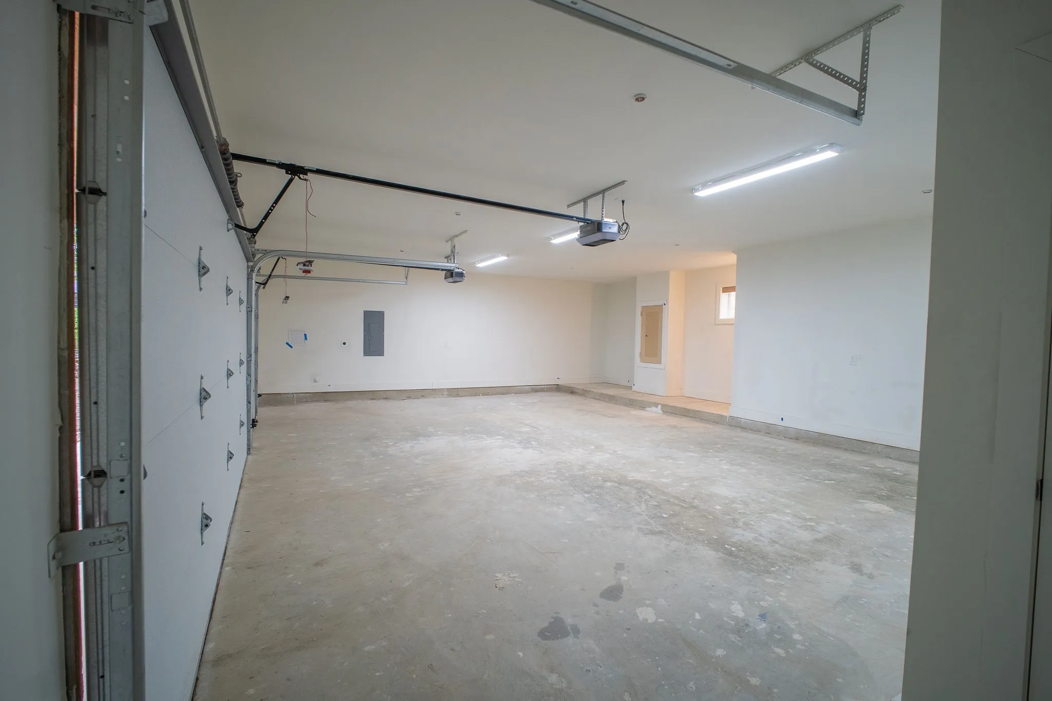 The garage features an open overhead door, a concrete floor, and overhead lighting fixtures