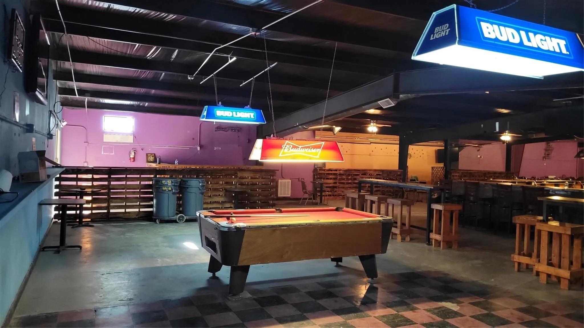 Expansive commercial space featuring a prominent pool table, exposed ceiling beams, and checkered flooring