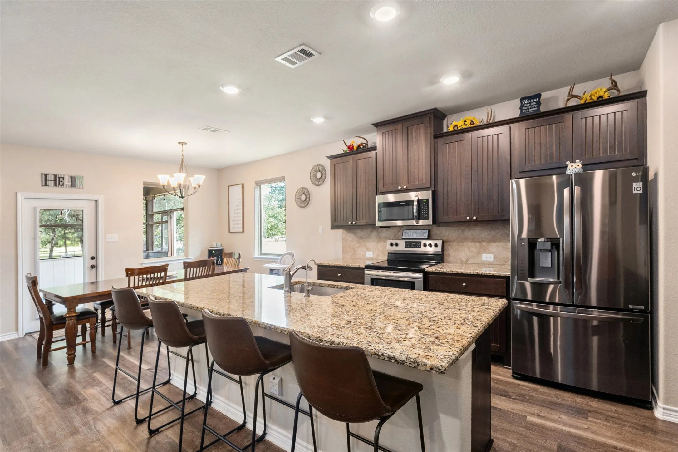 Open-concept kitchen featuring an oversized island with granite countertops, wood-finish flooring, and dark wood cabinetry